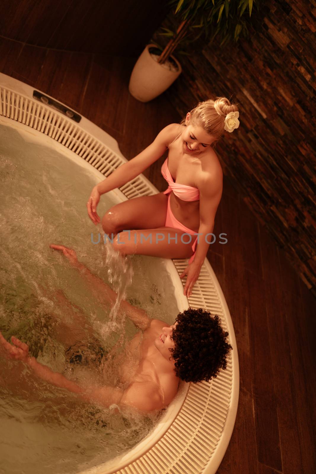 Beautiful young couple enjoying in a hot tub at the spa centre. Top view.