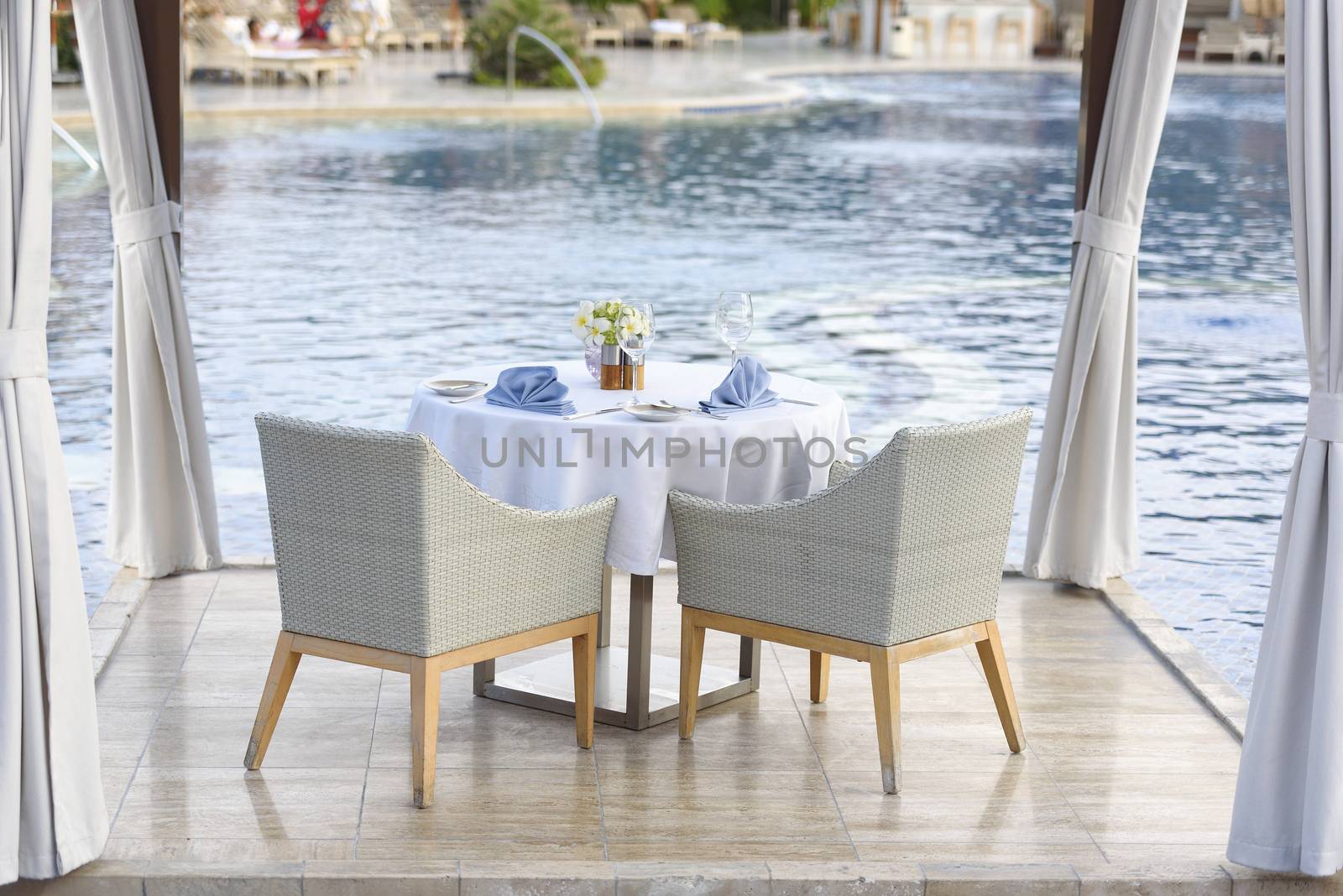 Dinner table for couple with white tablecloth and blue napkins by the pool. Romantic dinner by the pool. Dining table for couple
