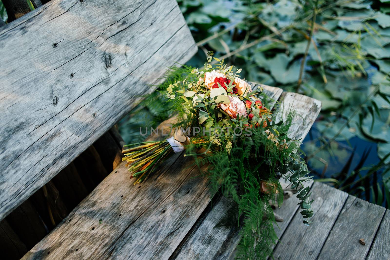 Lush wedding bouquet on a gray wooden bench near the water with water lily by d_duda