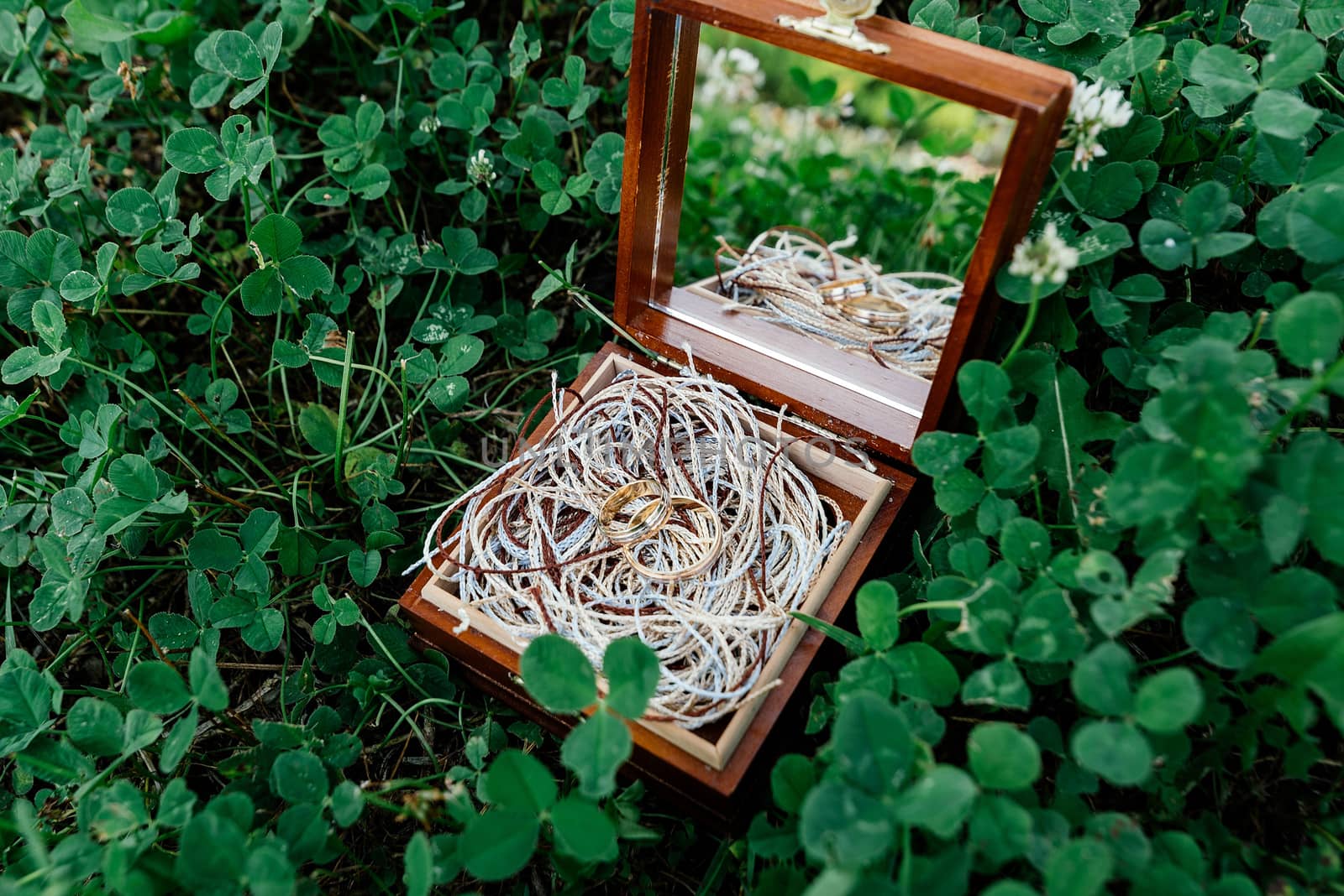 Golden wedding rings lie on the ropes in a wooden box with a mirror, which stands on the grass