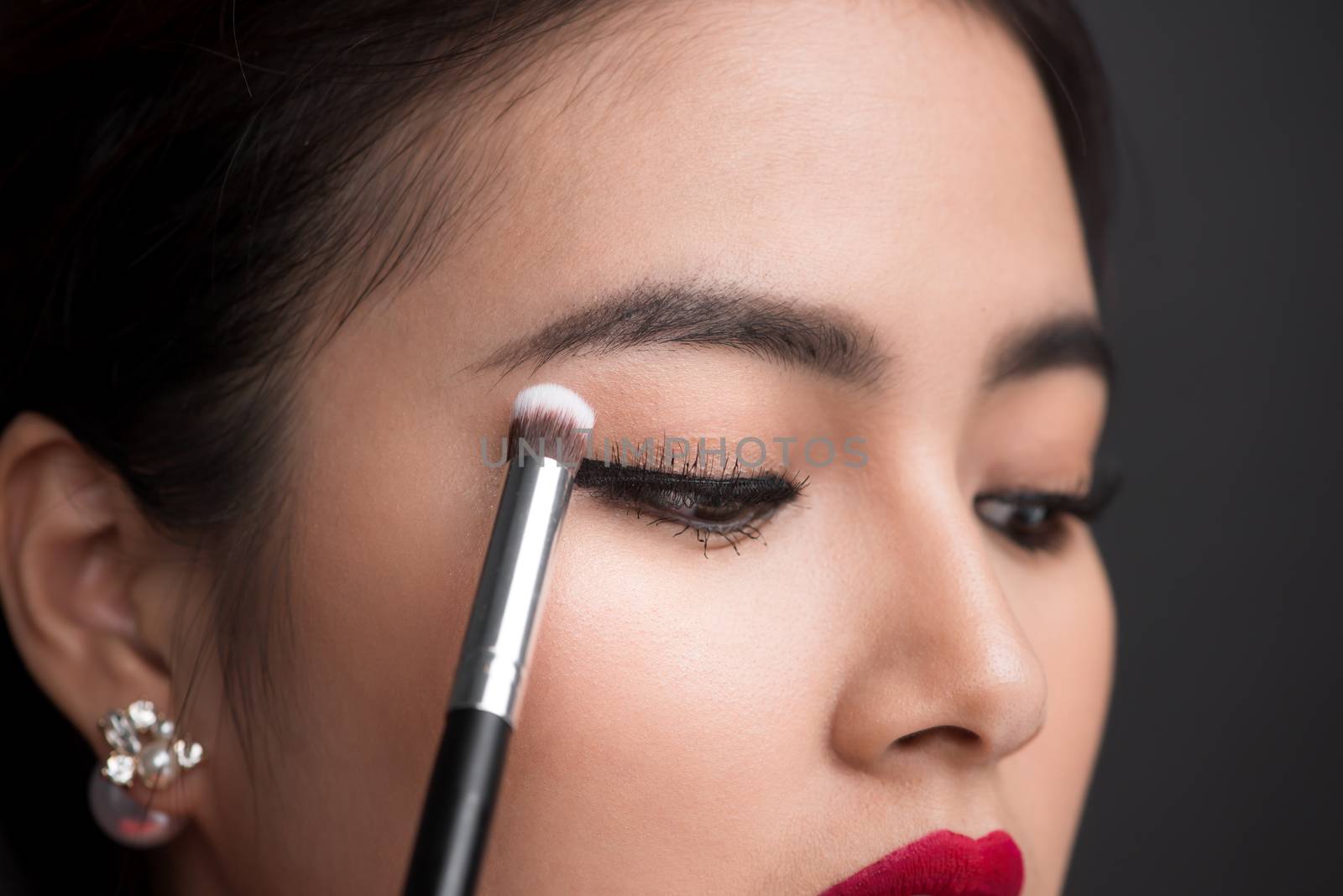 Close up of hand of asian woman applying eyeshadow on female eye by makidotvn