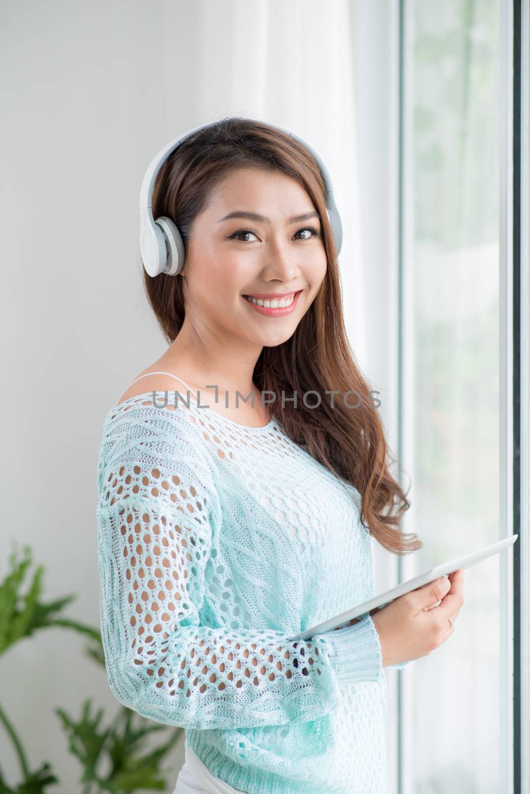 Asian woman enjoying view on windowsill and listening to music. by makidotvn