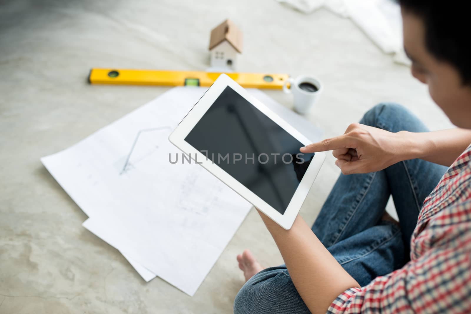 Young handsome male asian architect working at home using tablet on the floor.