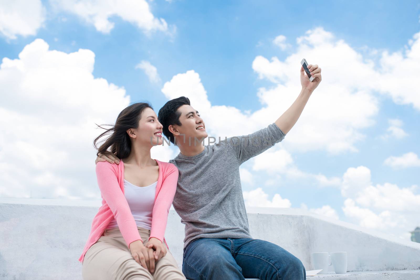 Young beautiful woman and asian man laugh against the dark blue sky with clouds