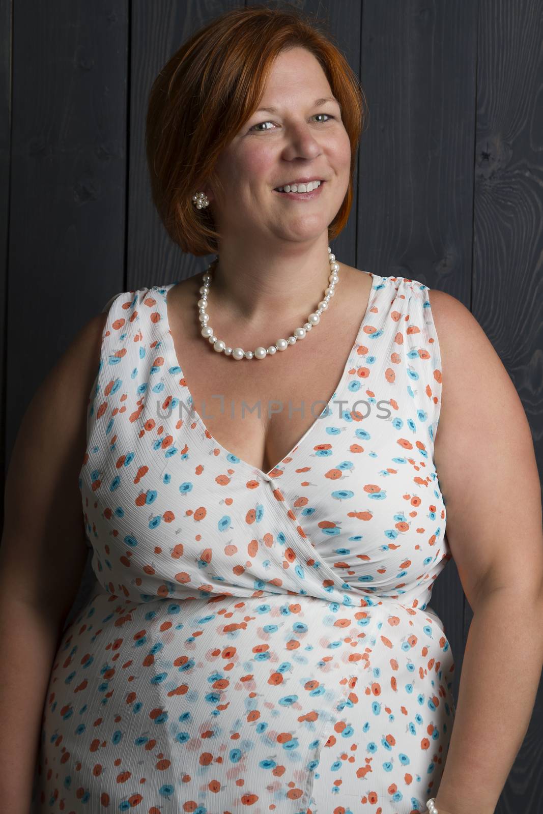forty something woman wearing a summer dress in front of a blue wood stain background