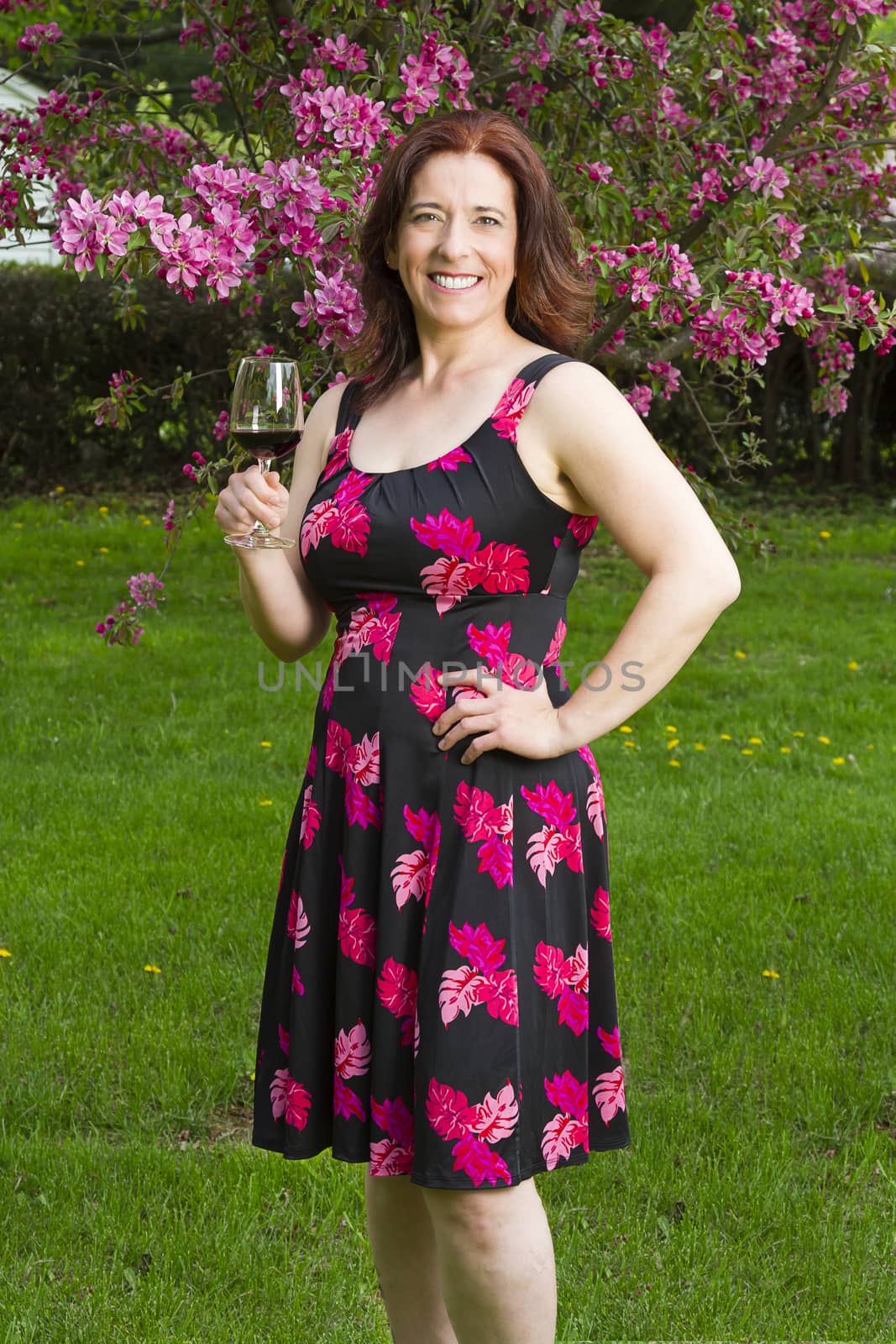 forty something woman wearing a summer dress, having a glass of red wine under a cherry tree