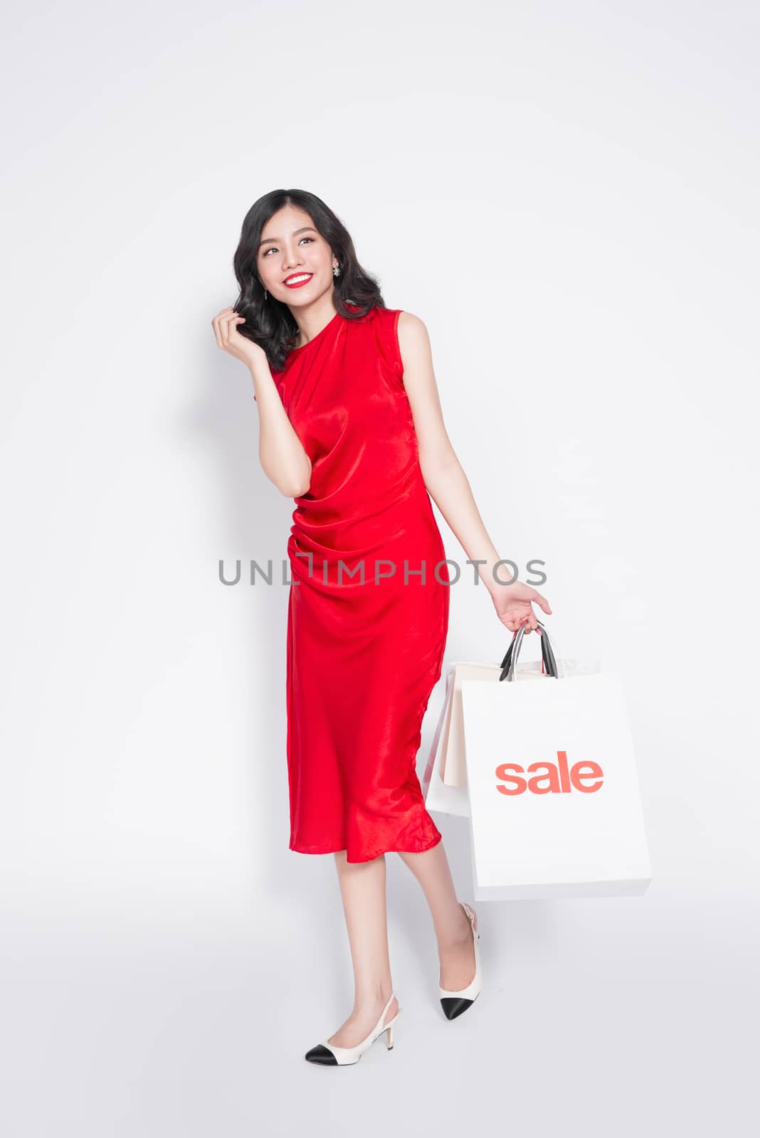 Full length of cheerful fashionable asian woman wearing a red dress with shopping bags