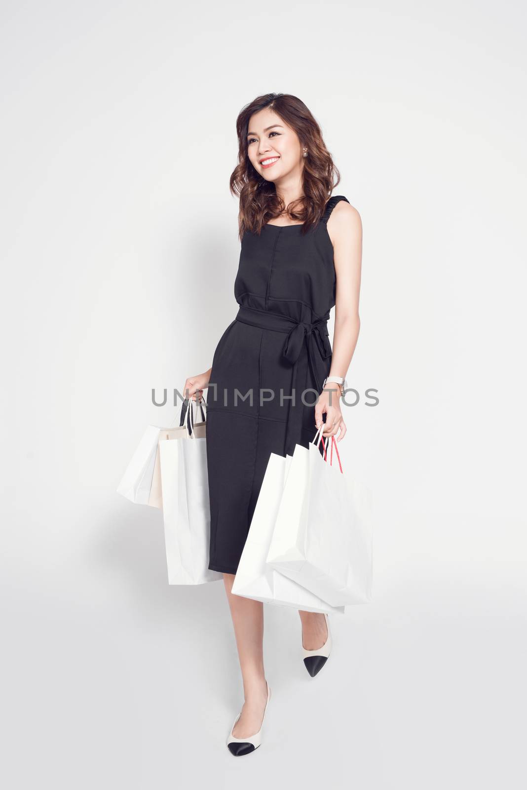 Beautiful asian woman wearing black dress with shopping bag standing over white.
