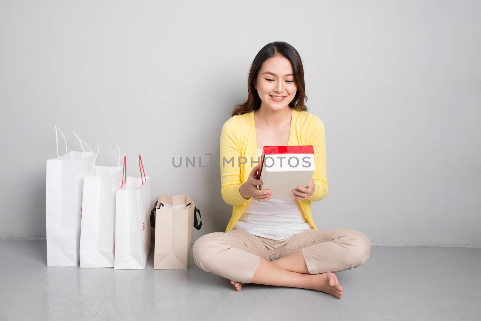 Young asian woman sitting besides row of shopping bags holding r by makidotvn