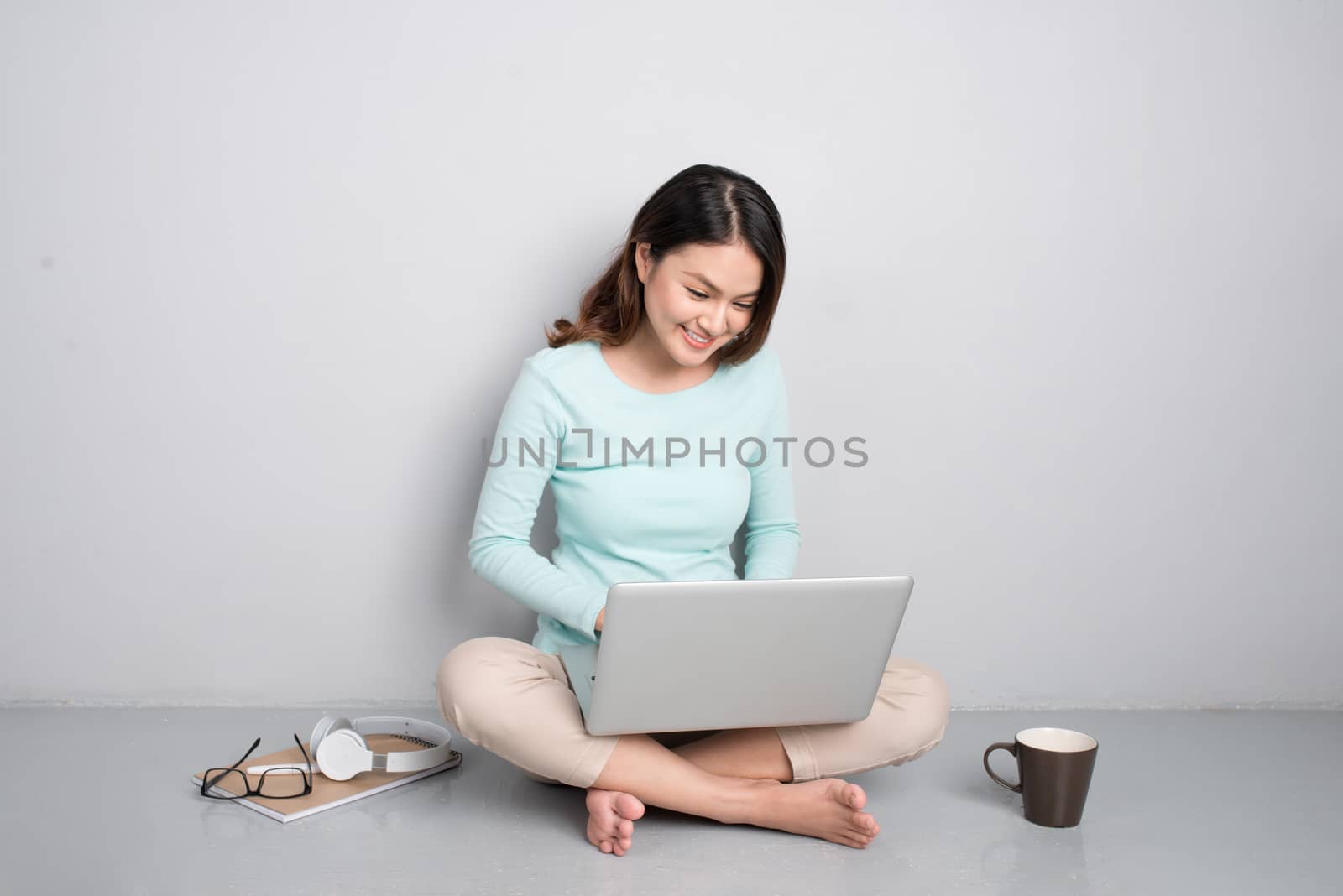 Happy casual beautiful asian woman working on a laptop sitting on floor at home.