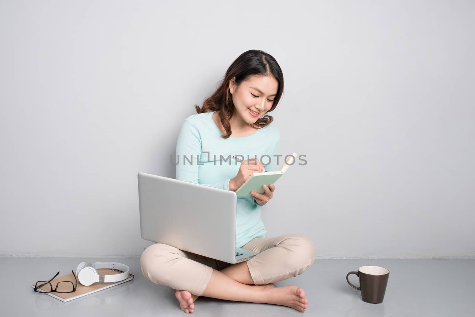 Happy casual beautiful asian woman working on a laptop sitting on floor at home.