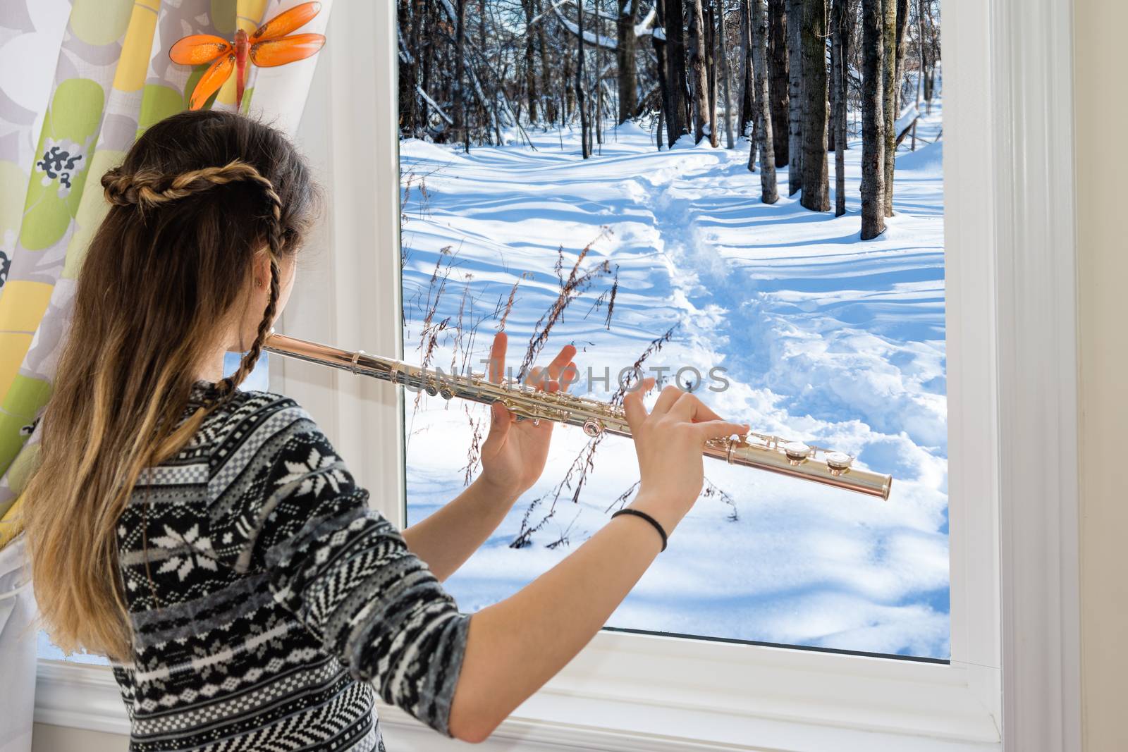 Winter sunny day, the girl is standing at the window and playing the flute
