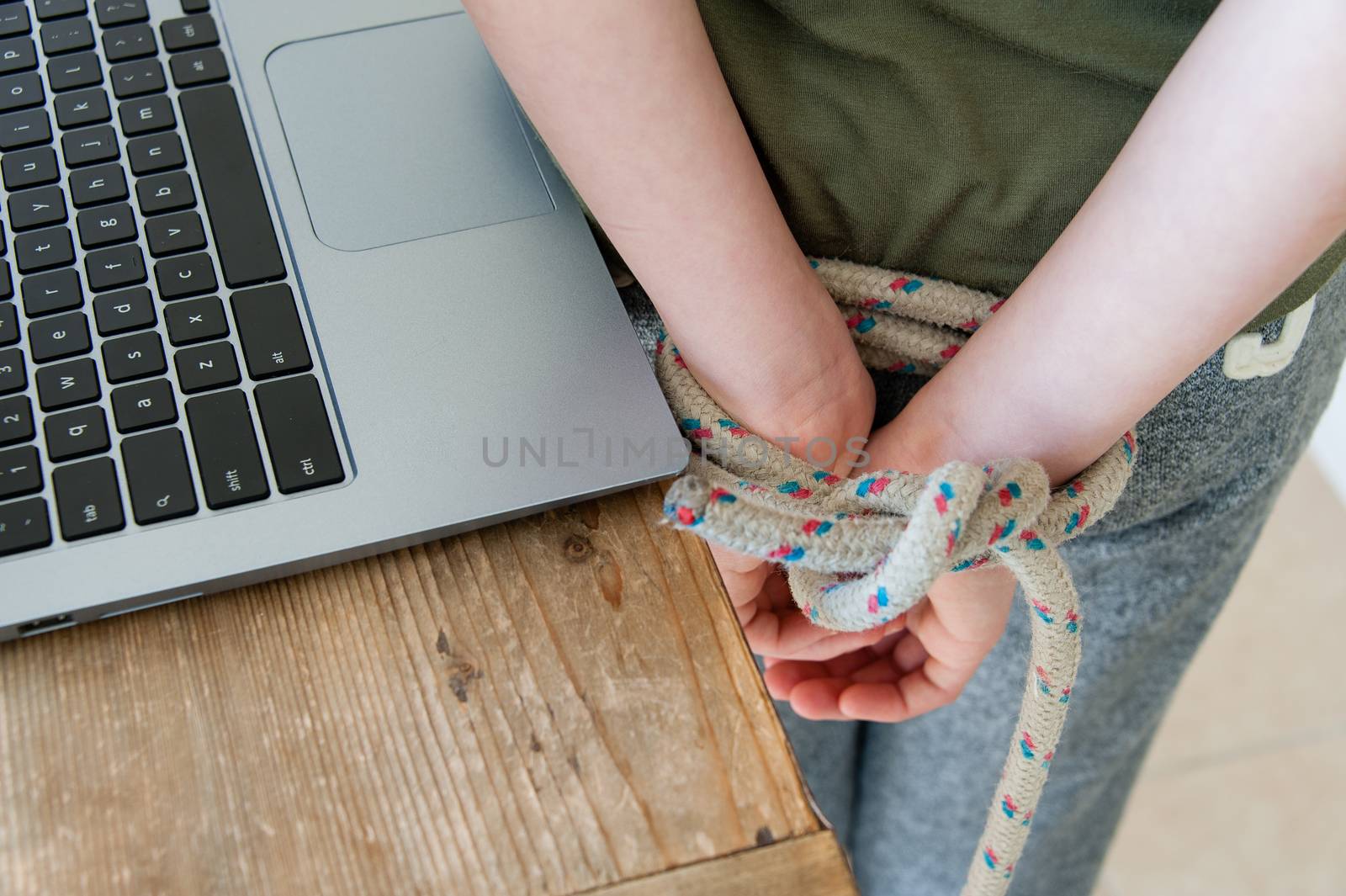 Hacker with  tied his hands behind his back standing near a table with a computer