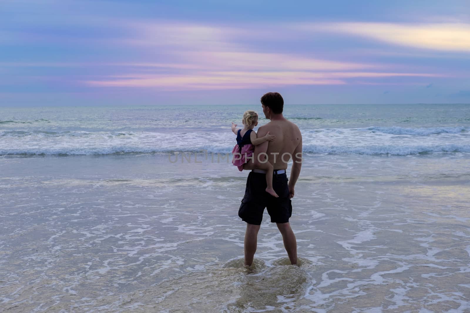 Father holds the daughter and shows her the beautiful spectacular sunset at the beach waves tide