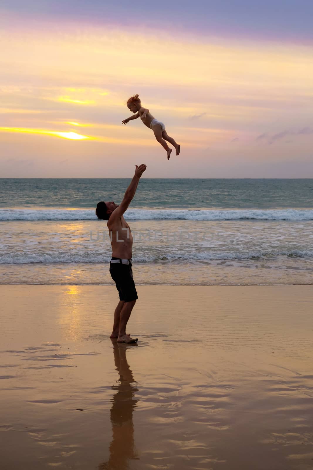 Father throws his daugter at the beach near the sea at the spect by rainfallsup