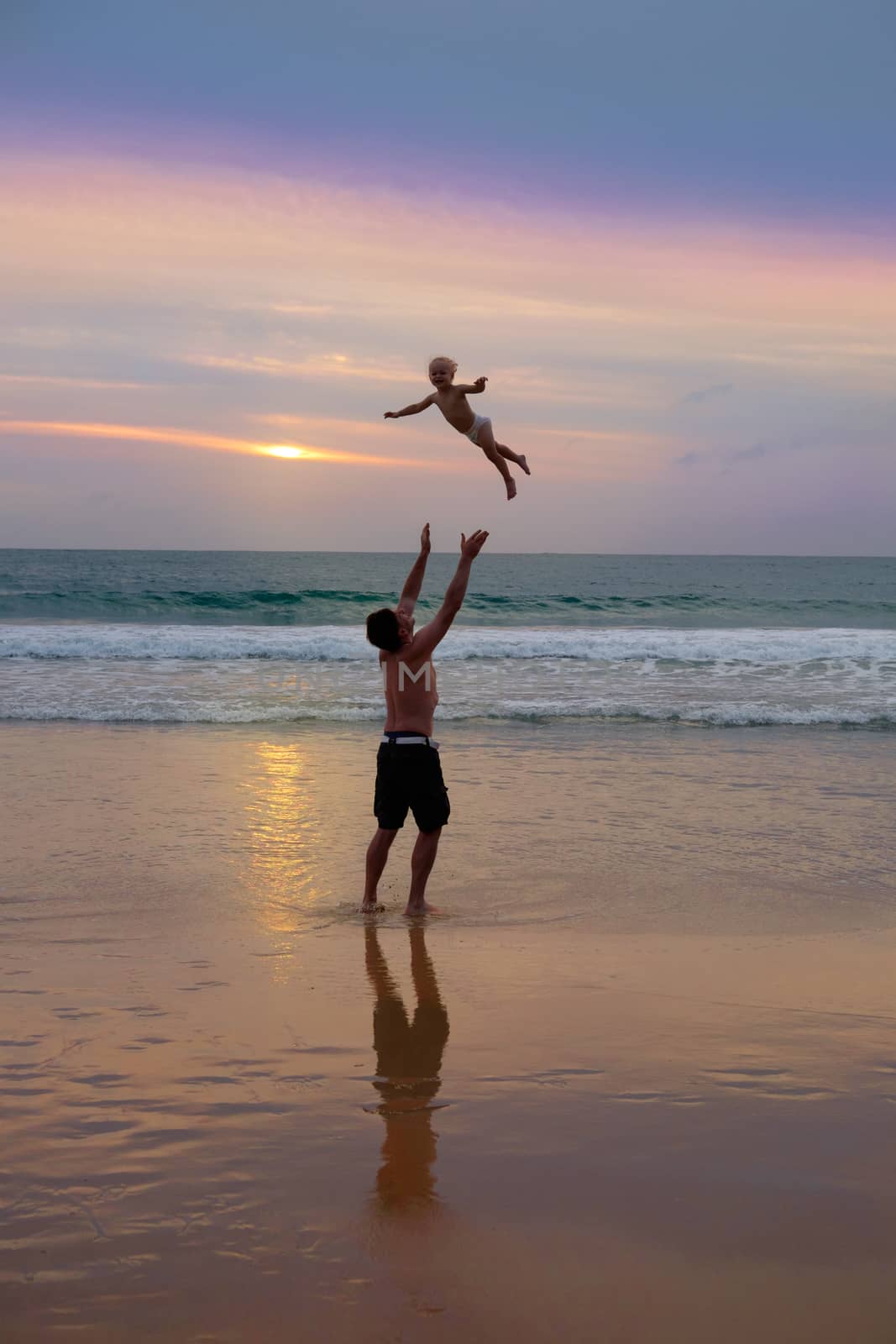 Father throws his daugter at the beach near the sea at the spectacular cloudy sunset