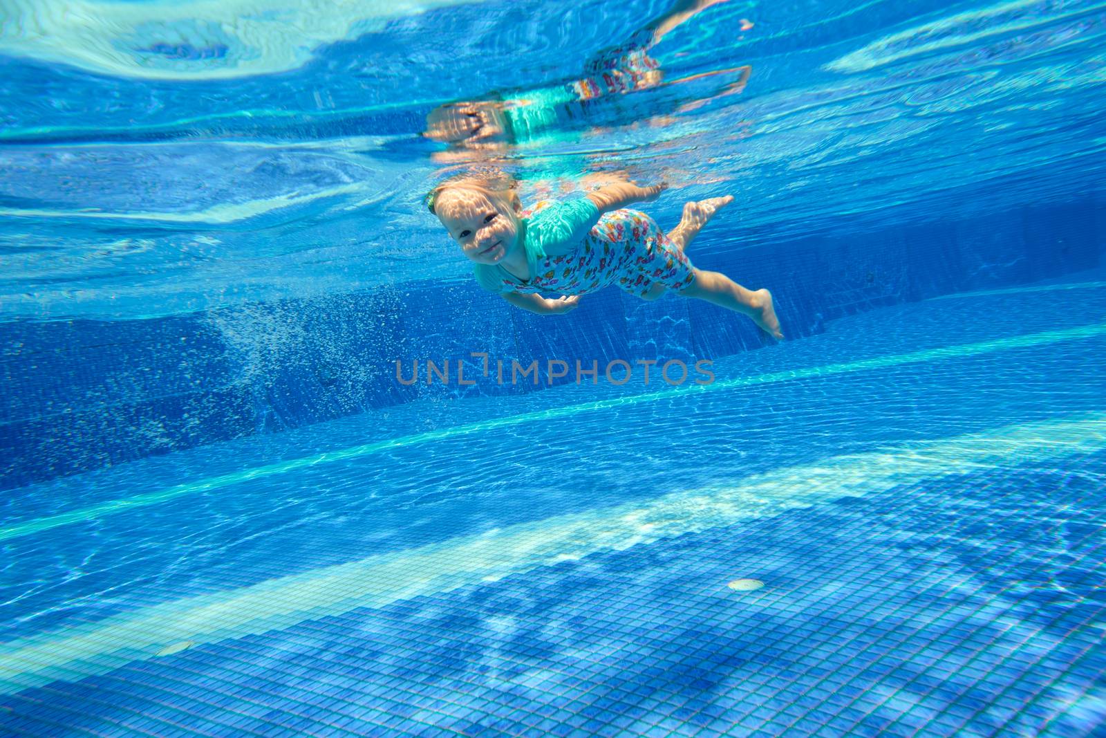 Little girl swimming underwater in the pool and smiling by rainfallsup