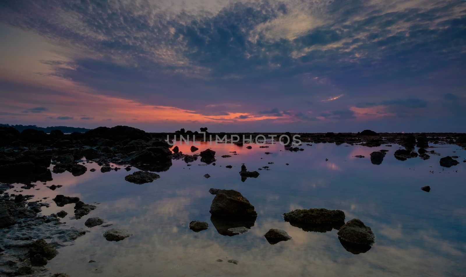 Colourful sunrise, stones and reflections in low tide ocean water