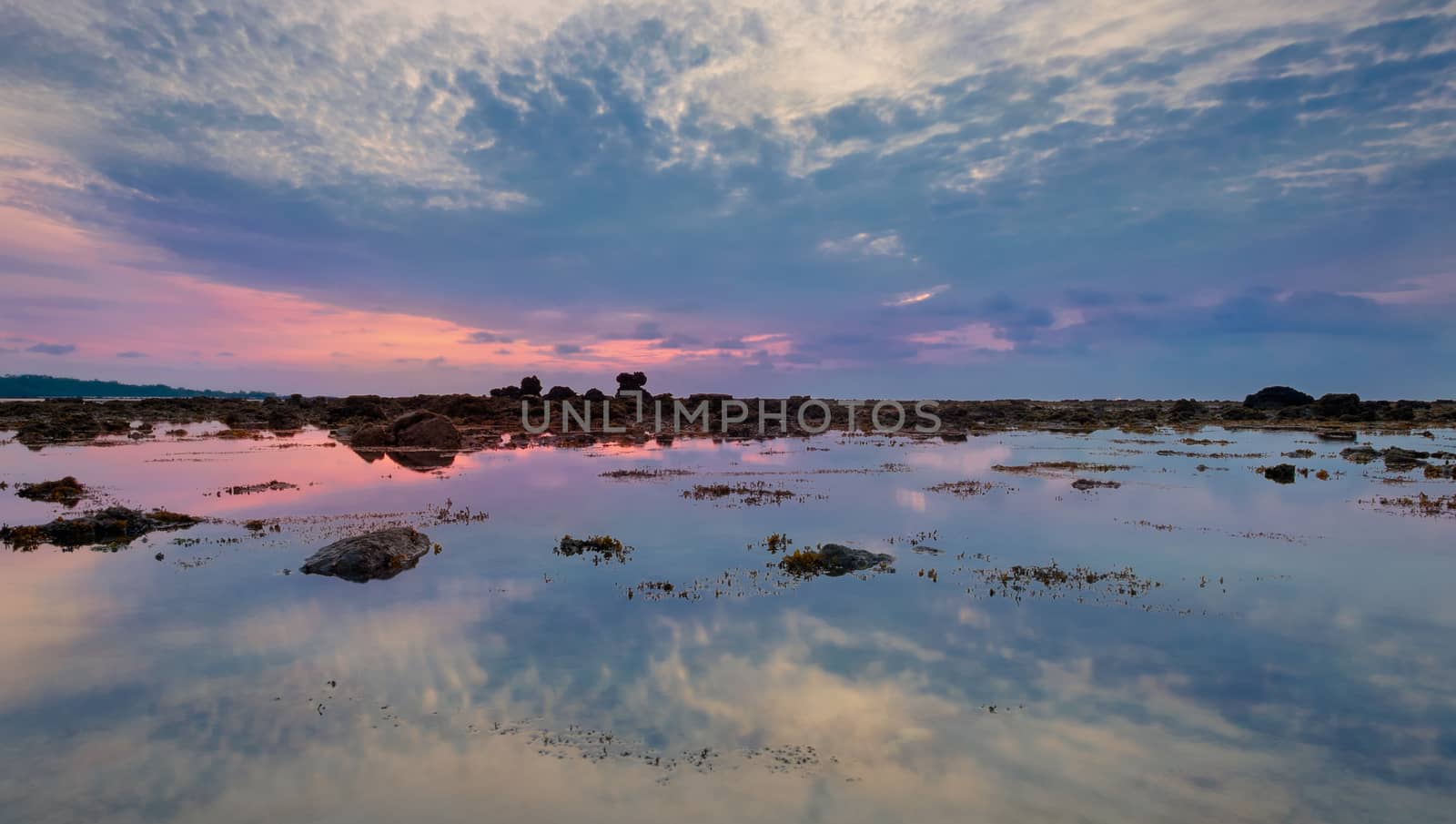Colourful sunrise, stones and reflections in low tide ocean water