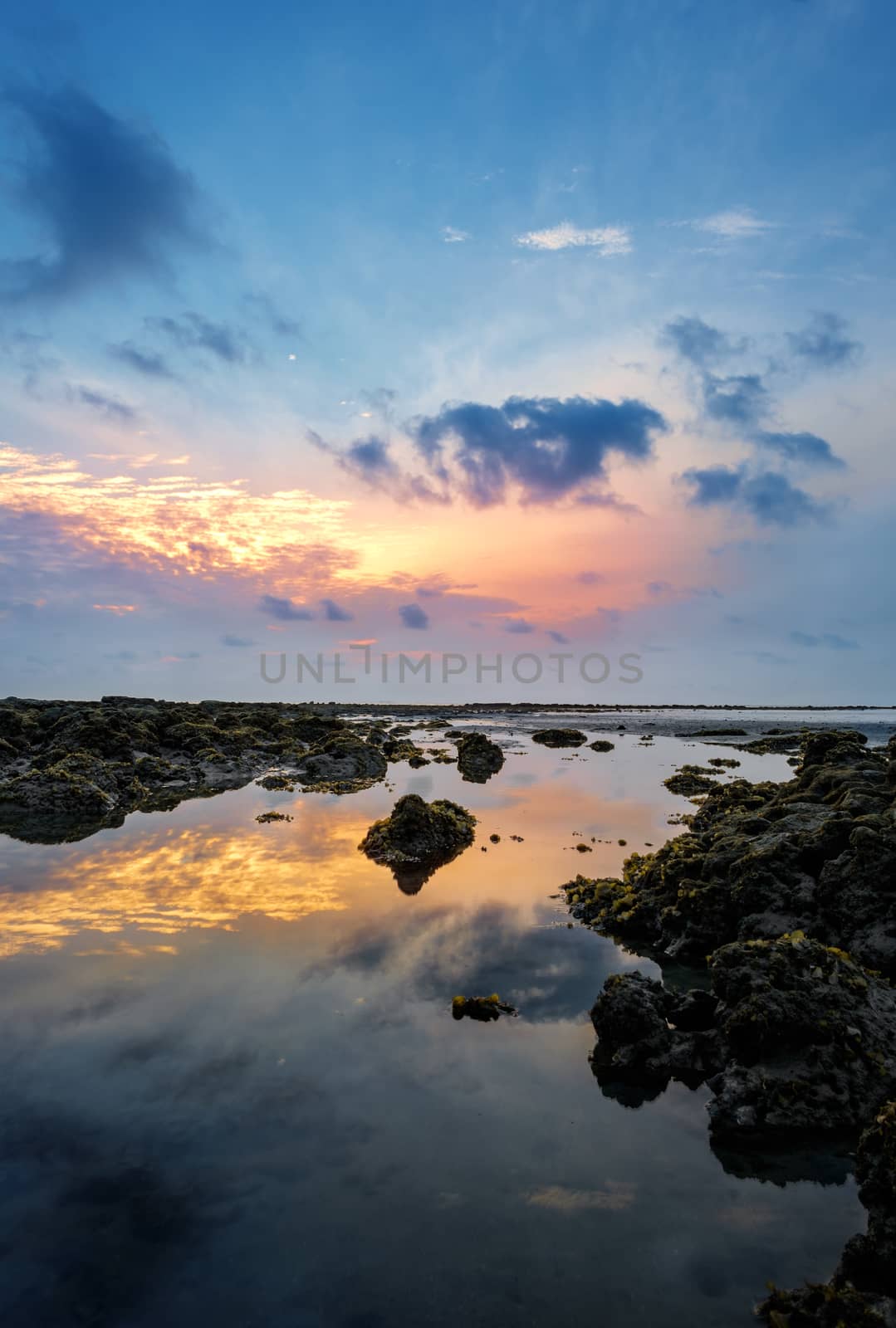 Colourful sunrise and stones in  low tide ocean water by rainfallsup