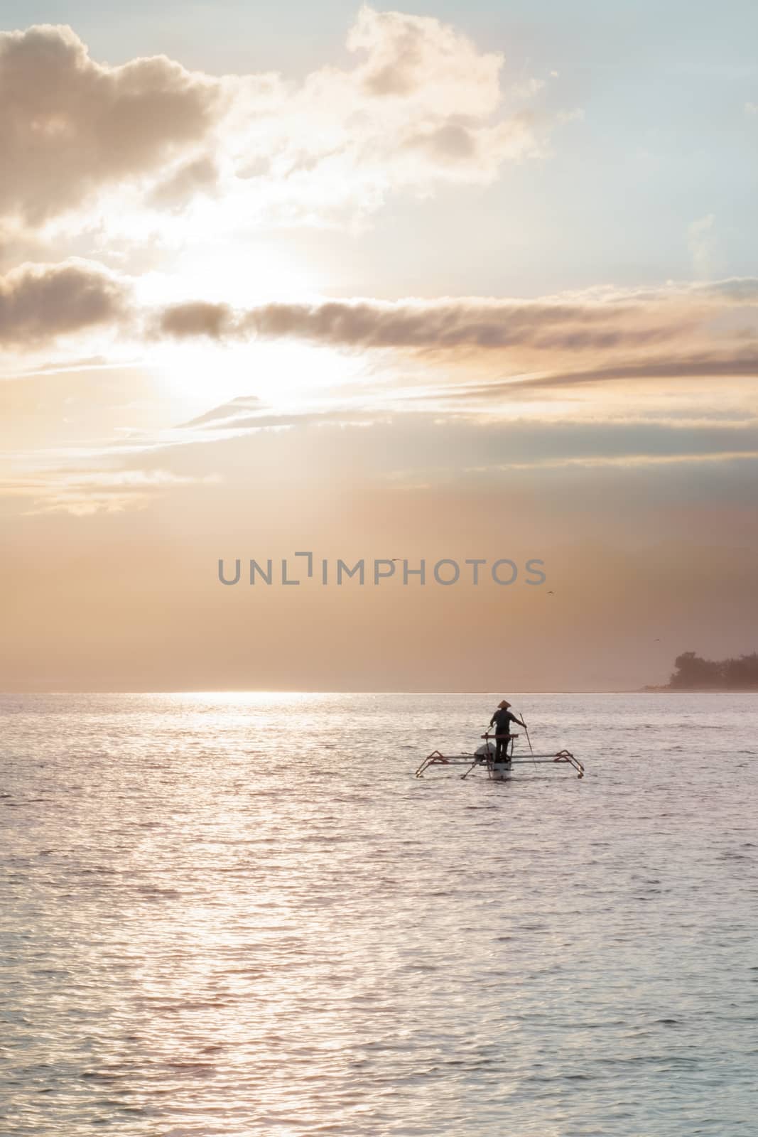 Indonesian fisherman in wide conical hat goes with his catamaran into pink sunrise by rainfallsup