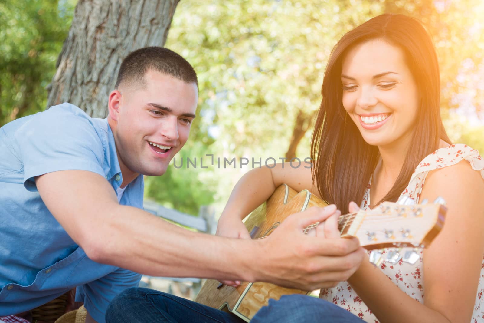 Handsome Young Man Teaching Mixed Race Girl to Play Guitar at the Park.