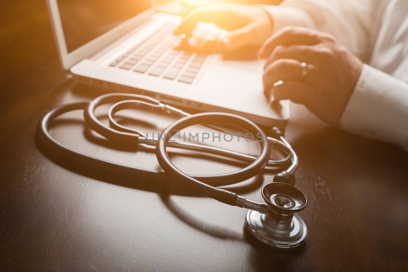 Medical Stethoscope Resting on Desk As Male Hands Type on Computer Keyboard. by Feverpitched