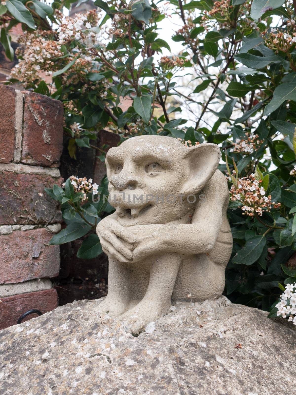 a strange goblin gremlin concrete statue on a pillar outside with fangs and big ears creepy scary odd