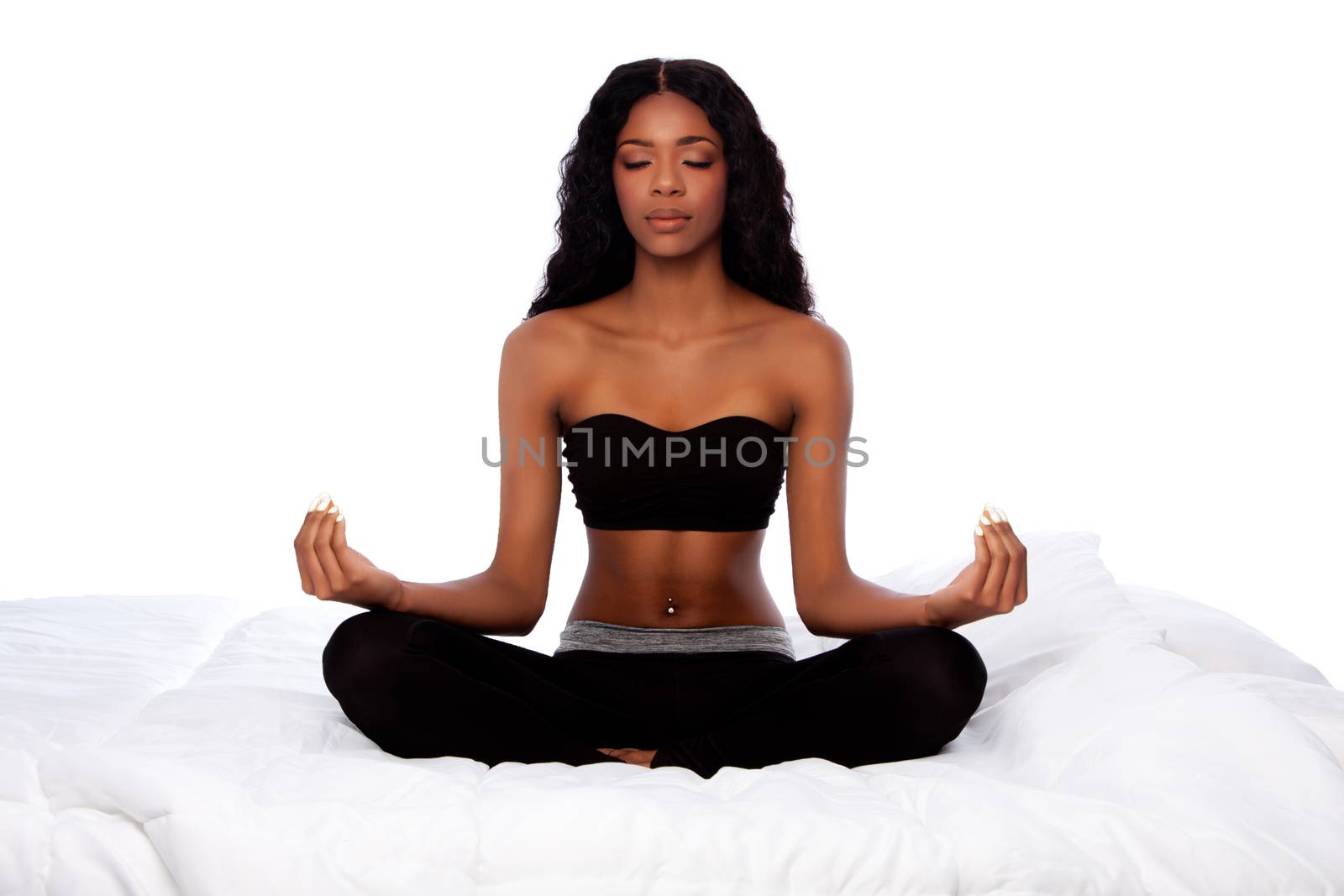 Beautiful woman sitting in lotus yoga pose on bed by phakimata