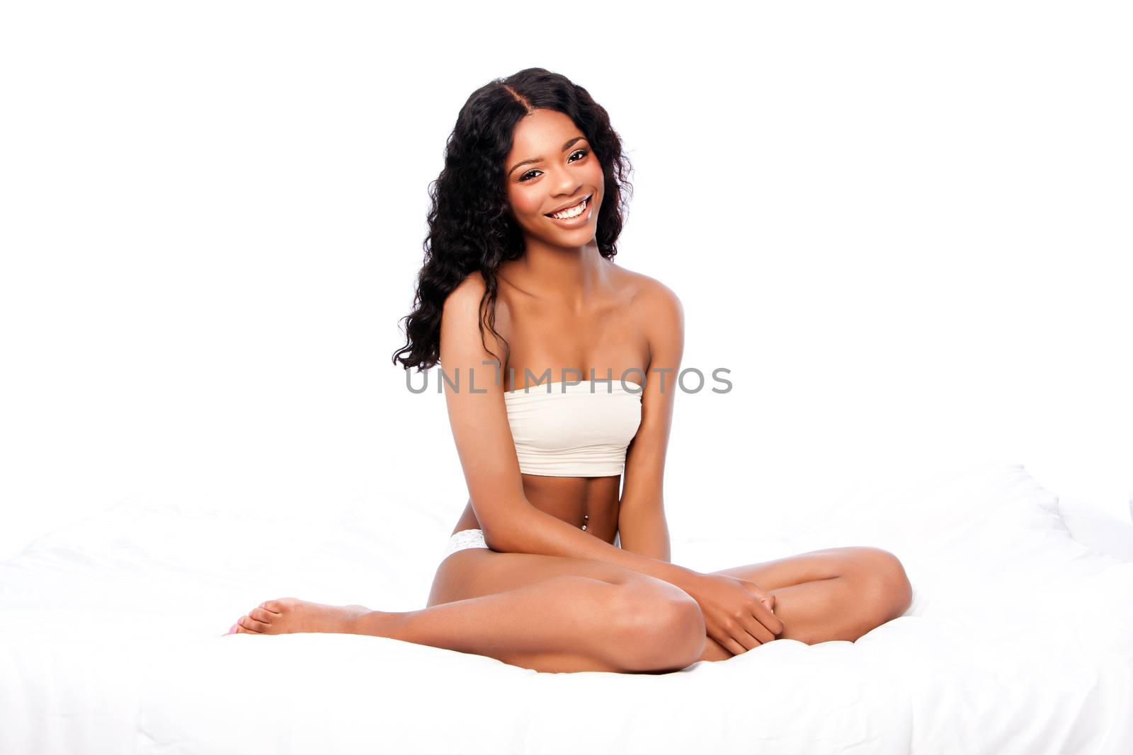 Beautiful attractive happy smiling African woman with curly hair sitting on fluffy soft bed in white.