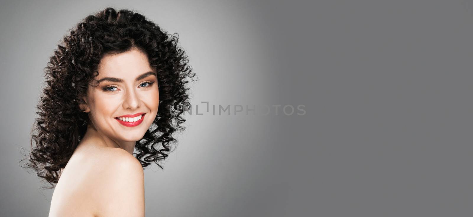 Portrait of amazing beautiful smiling woman with curly hair on gray background with copy space