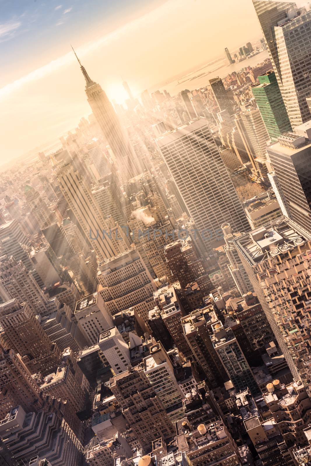 New York City. Manhattan downtown skyline with illuminated Empire State Building and skyscrapers at sunset. Vertical composition. Warm evening colors. Sunbeams and lens flare.