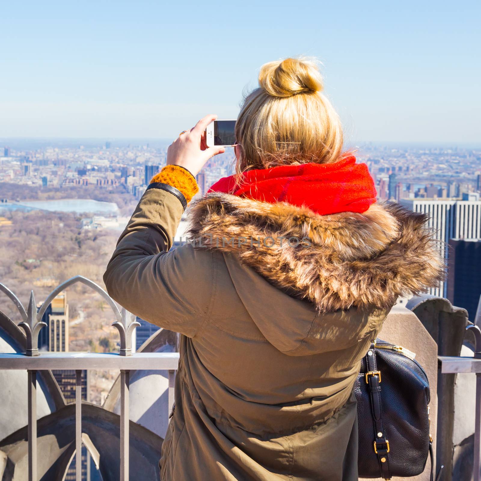 Female tourist taking a photo of New York City panorama with her smart phone from observation deck.