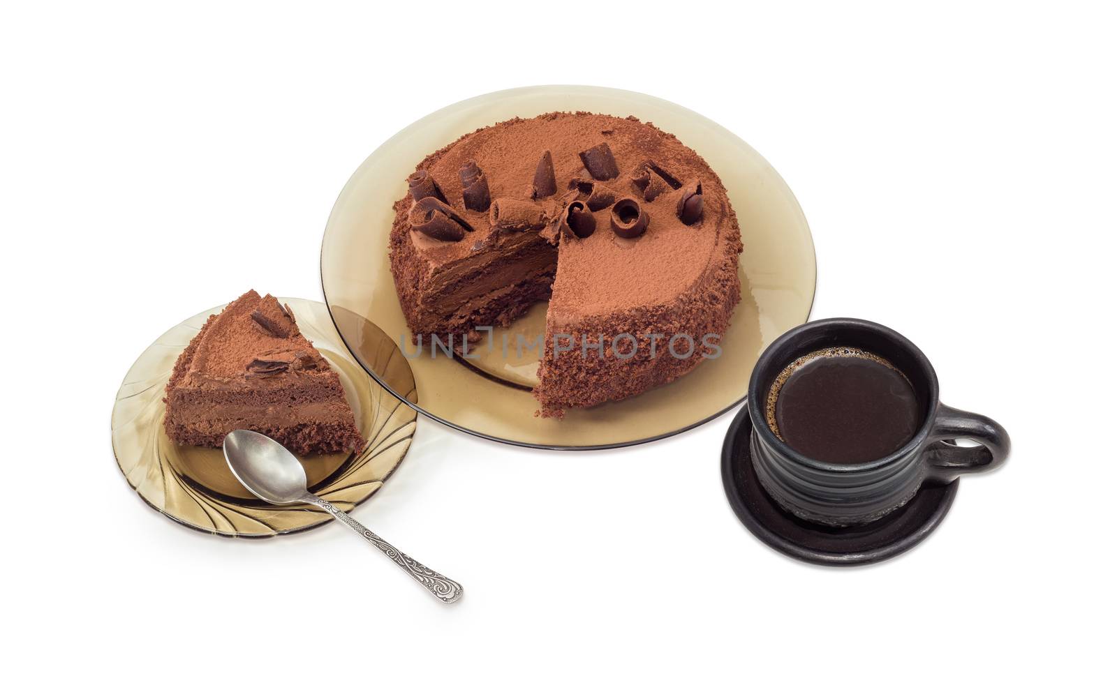 Partly sliced chocolate cake decorated with chocolate chips and cocoa powder on the glass dish, slice cake on saucer with spoon and black coffee in black ceramic cup on a light background
