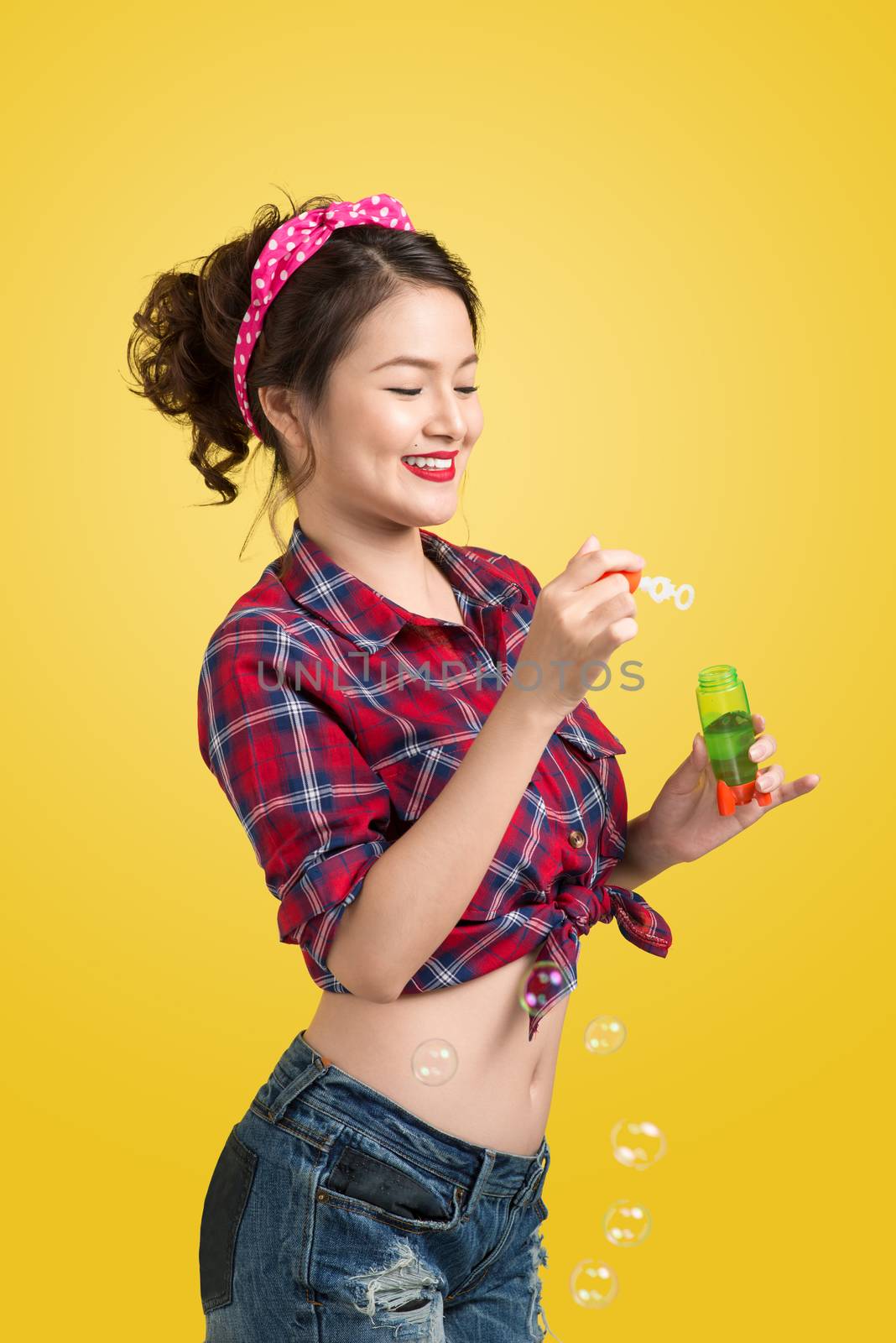 Pinup model blowing soap bubbles over yellow background.