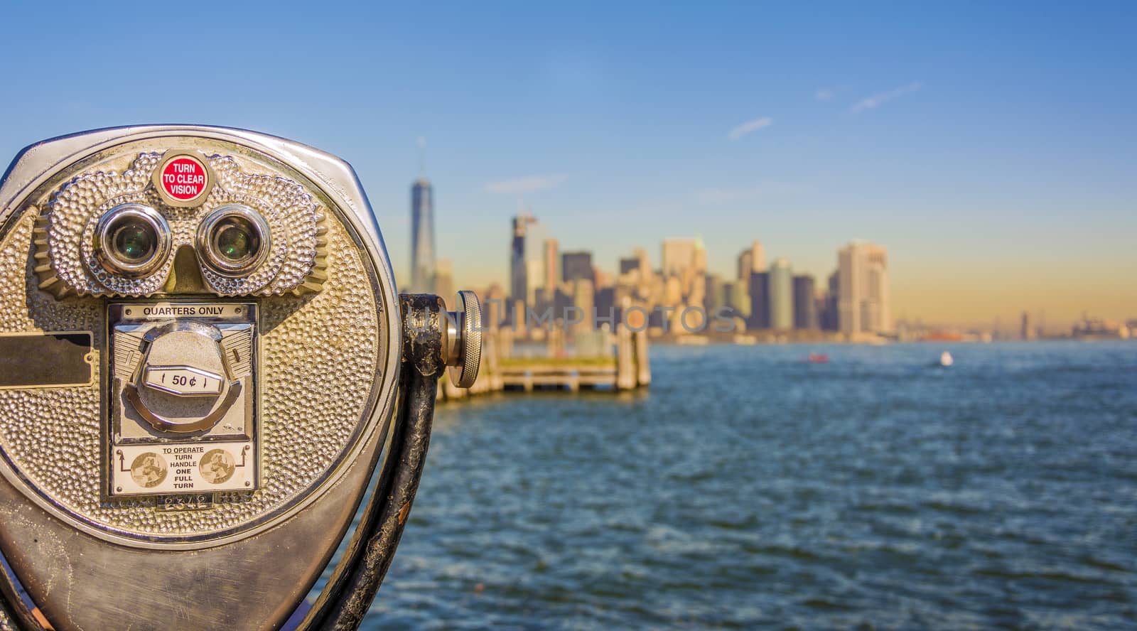 Close up of tower viewer binoculars with blurred New York City skyline in the background on Liberty Island. New York City Harbor and Lower Manhattan skyline on a bright sunny day, shallow DoF.