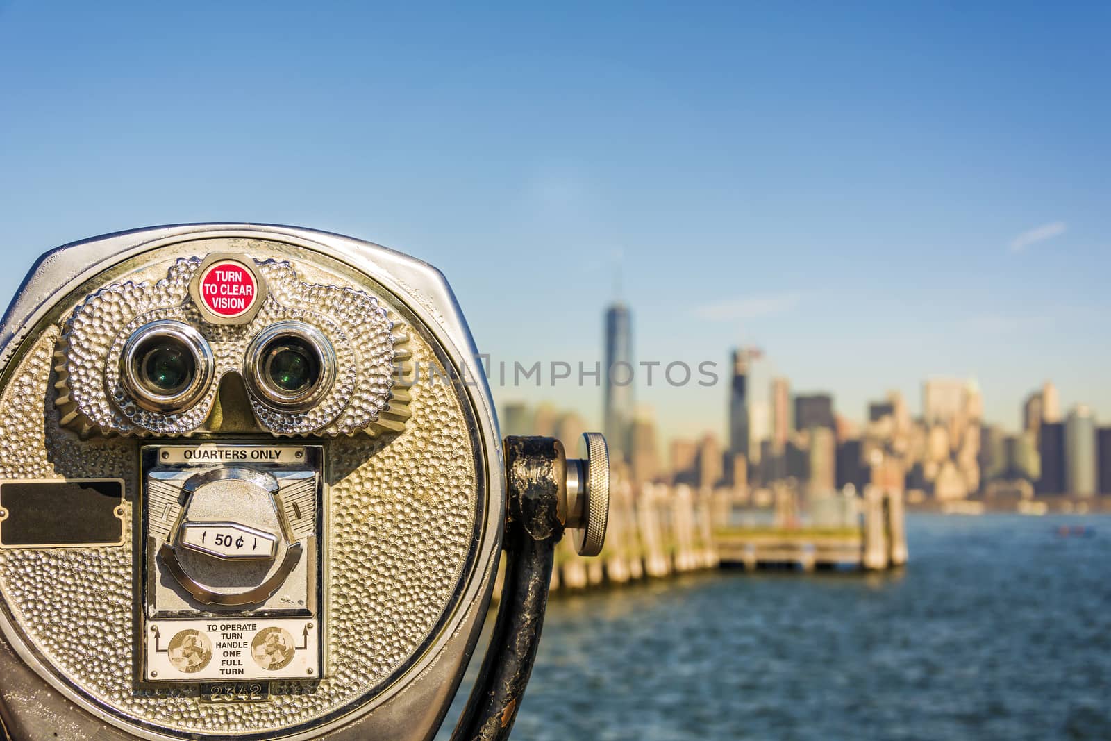 Close up of tower viewer binoculars with blurred New York City skyline in the background on Liberty Island. New York City Harbor and Lower Manhattan skyline on a bright sunny day, shallow DoF.