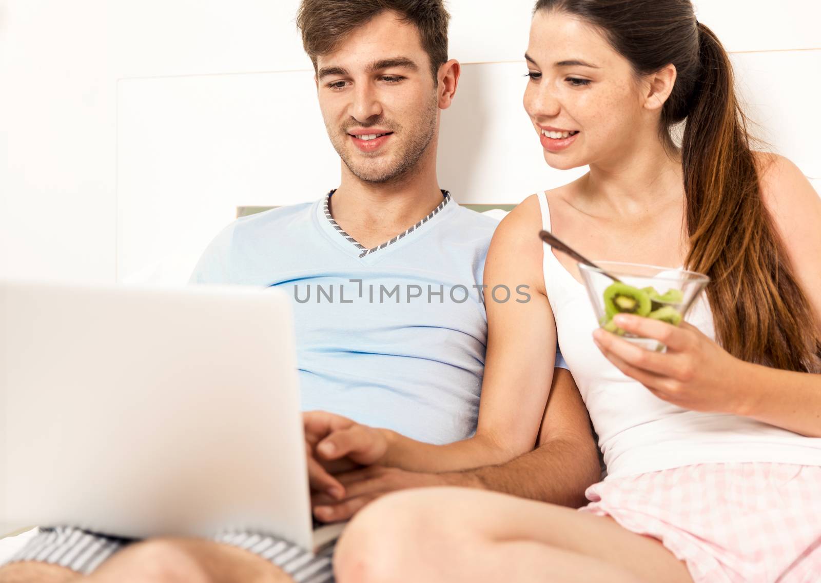 Young couple siting on bed working and eating breakfast