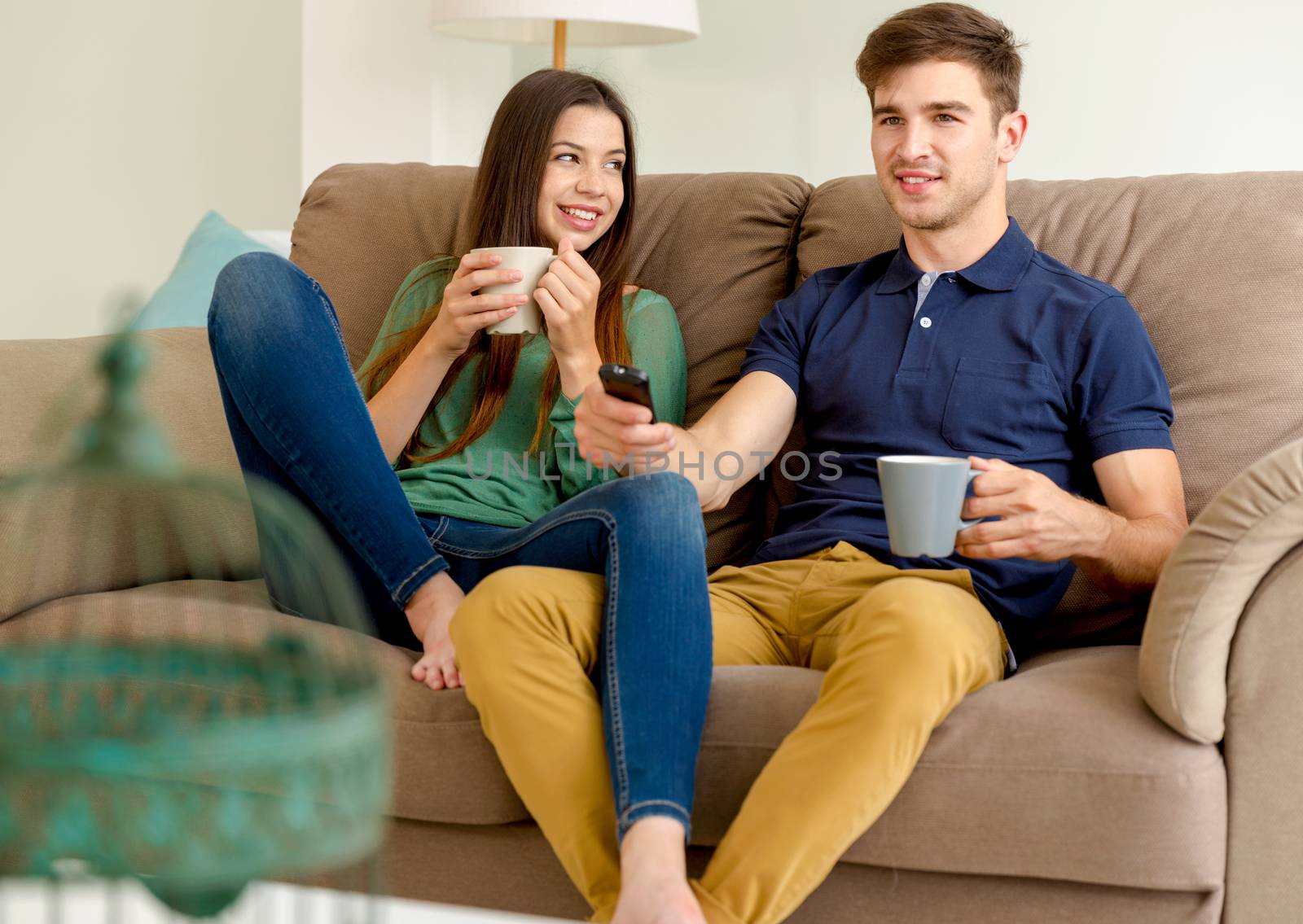 Young couple on the sofa drinking coffee while watching tv