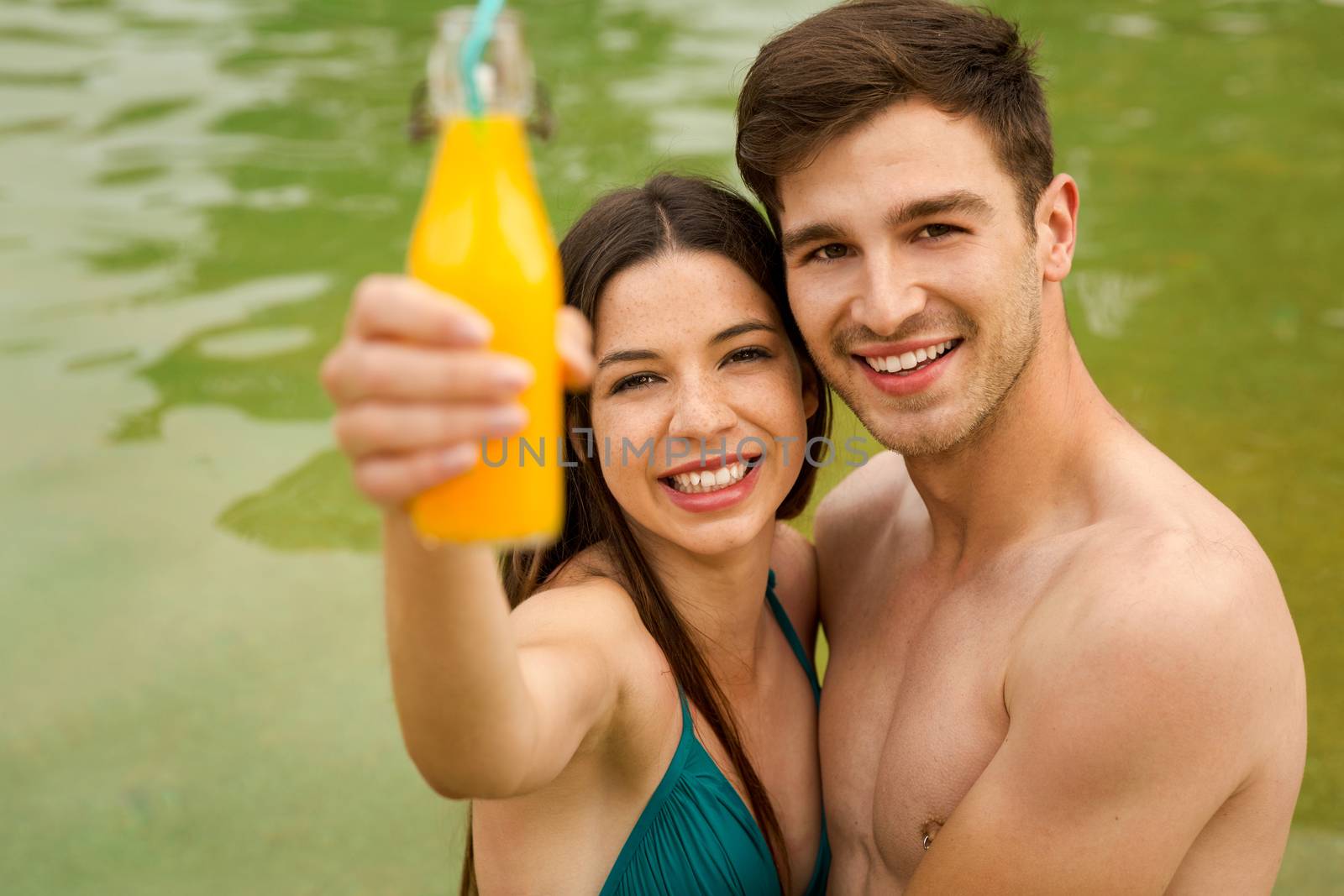 Young couple inside the pool and drinking natural juices