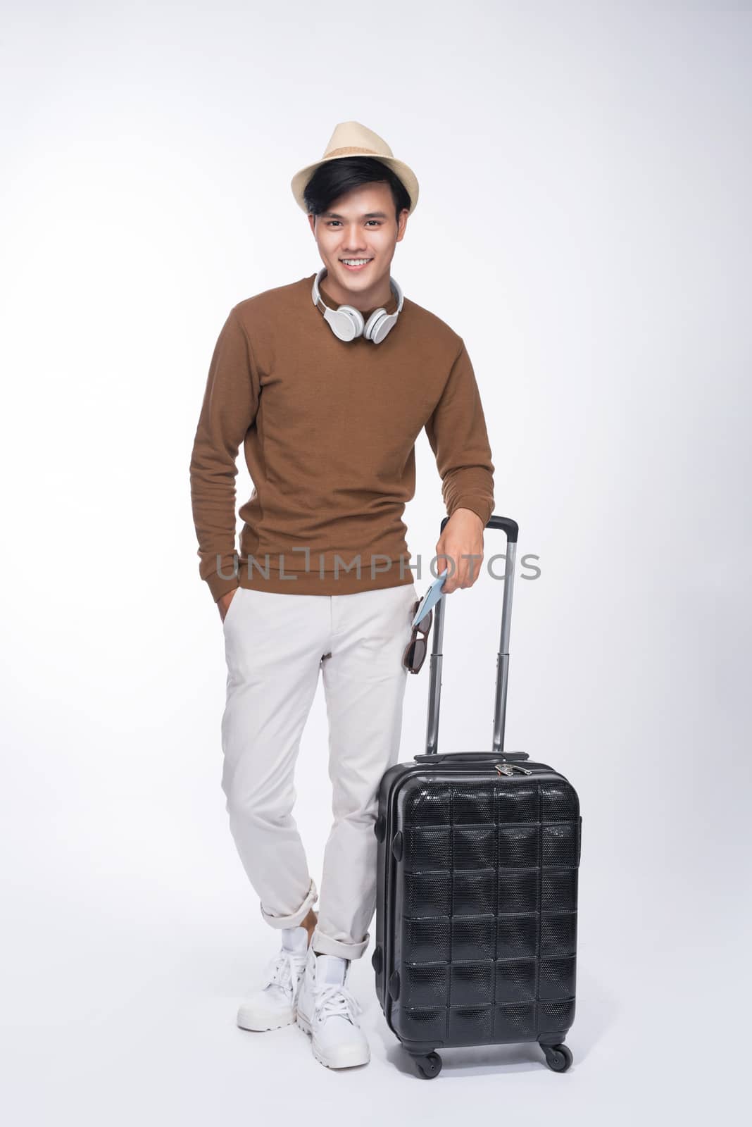 Full length of young tourist asian man holding passport with suitcase over grey background
