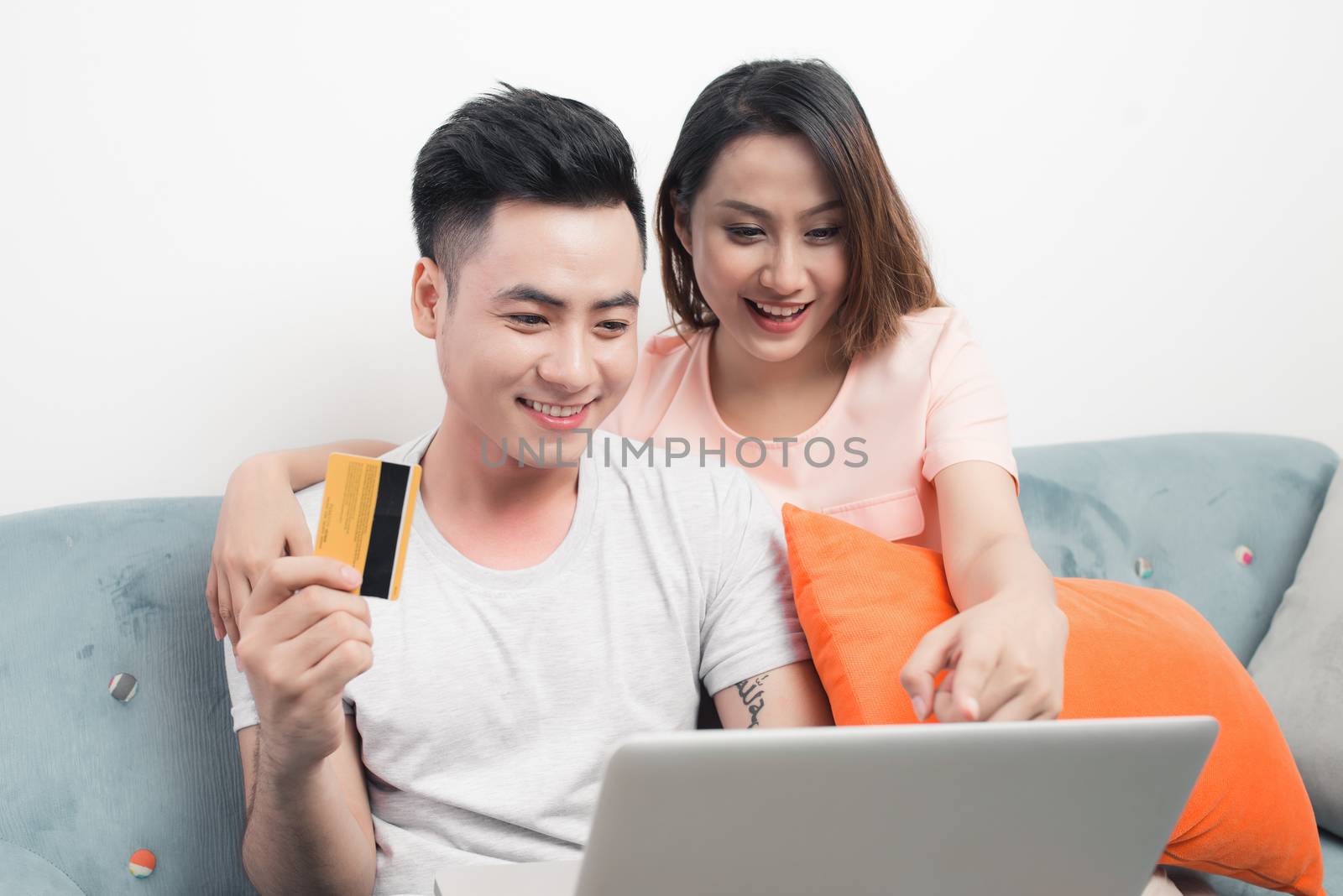 Young asian couple surfing on internet and shopping with laptop. Modern white apartment in background