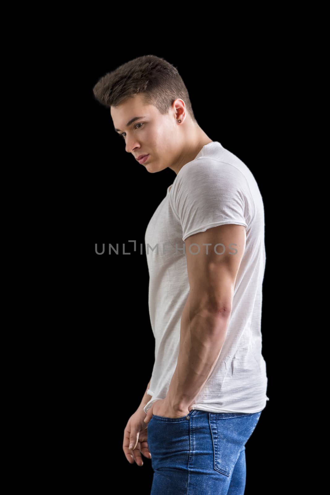 Handsome young muscular man looking down to a side, in studio shot isolated on black background