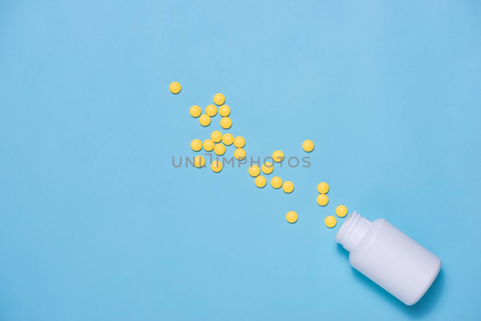 Yellow pills with bottle on blue background.