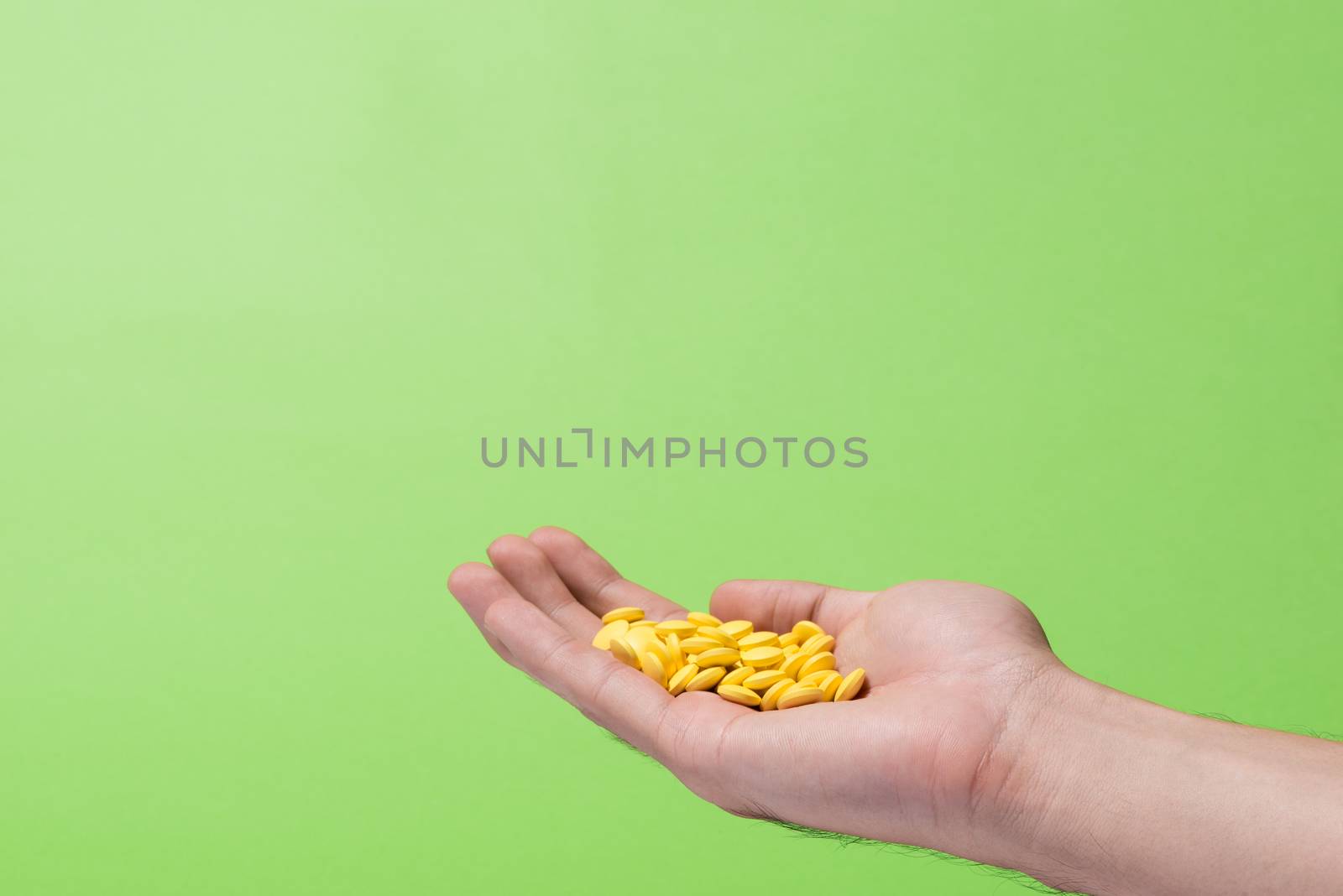 Yellow pills in hand on green background.