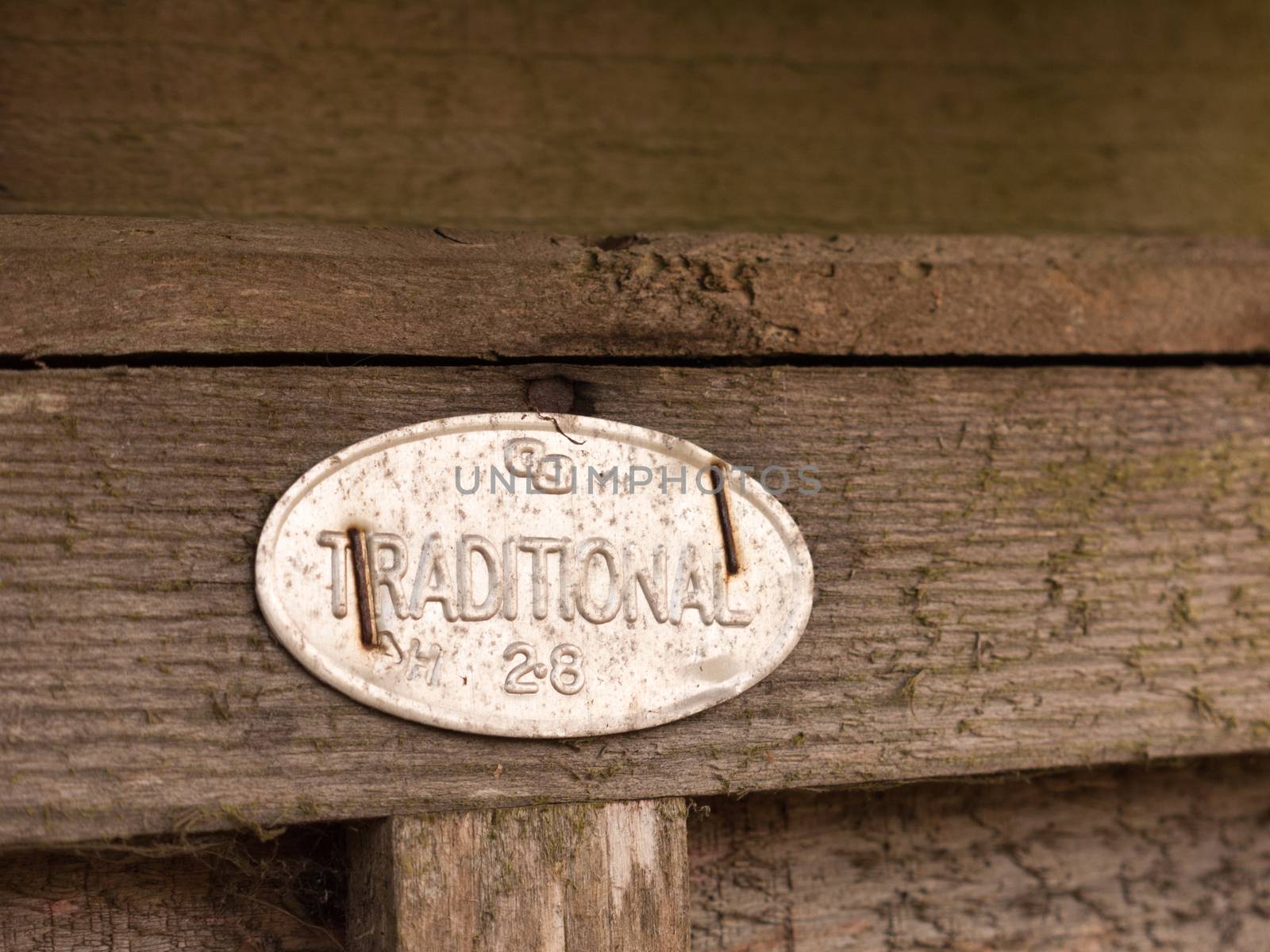 a metal sign stapled to a fence saying traditional oval shining retro vintage wooden background in light detail macro isolated