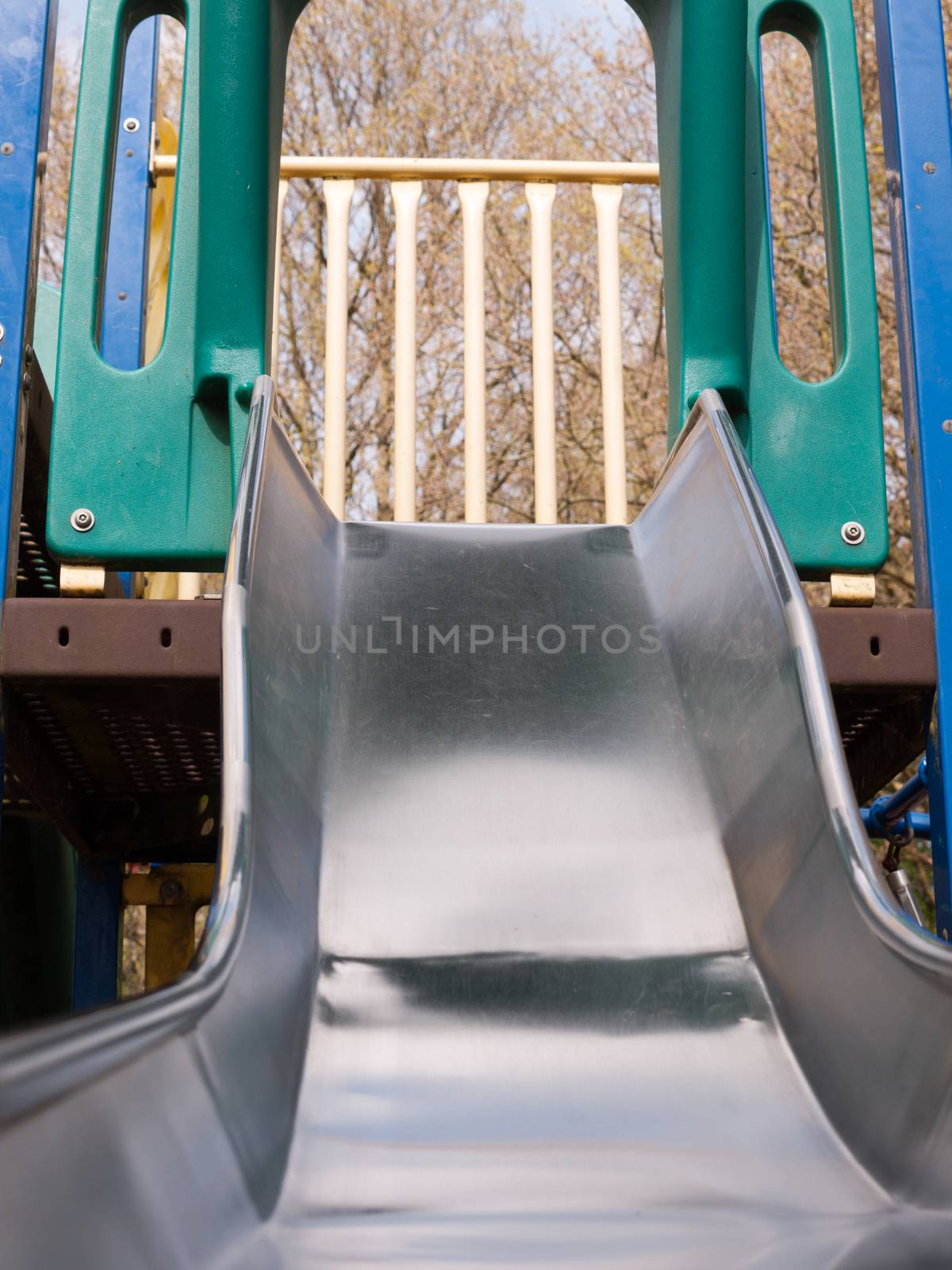 a close up shot of a metal slide in a child's playground with bark wooden chips for safety, accident, no people shining metal, dangerous and fun for children and parents in summer and spring