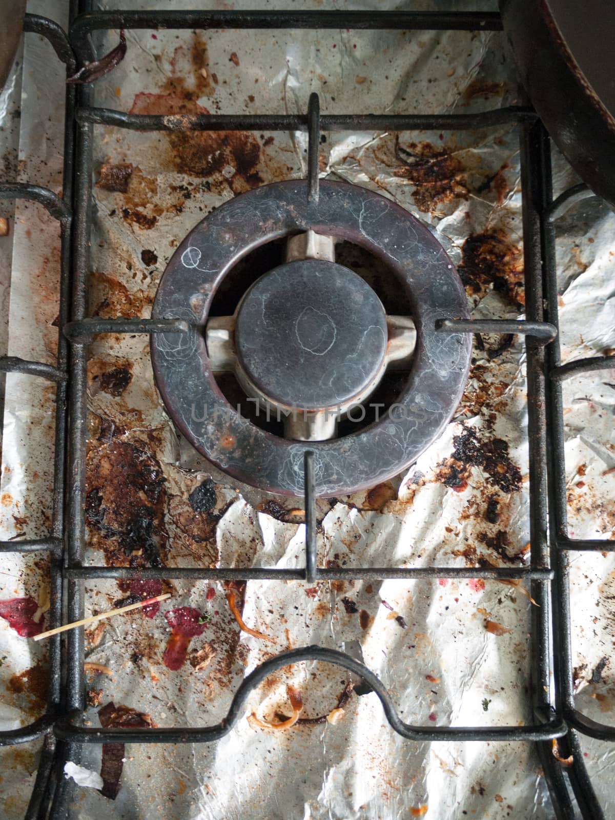 The Dirty and Grimy and Rusted Top of Gas Cooker Hob with Bits of Foil Underneath the Metal with Bits of Food and High Detaul Shining with Cracks and Blemishes and Stains Used for Cooking with Pans in UK in Kitchen