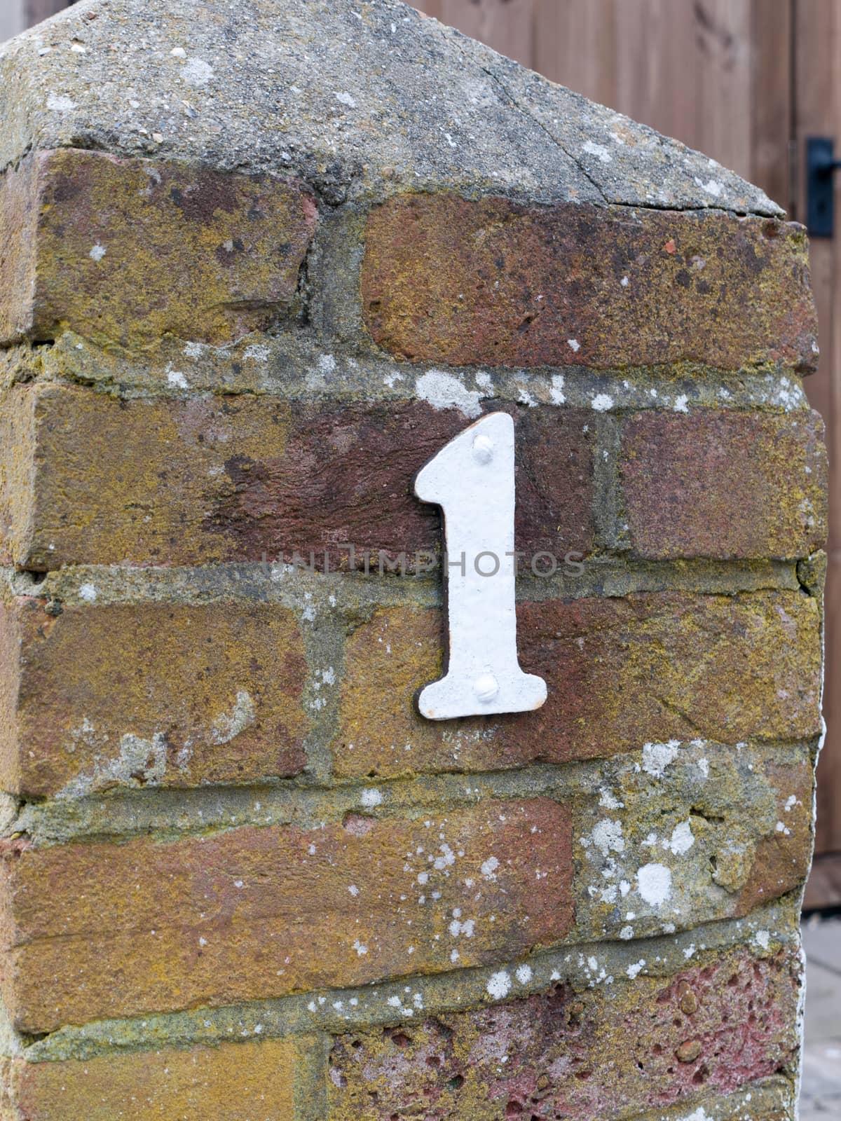 a white single number plate of 1 outside on the wall house wall brick own first