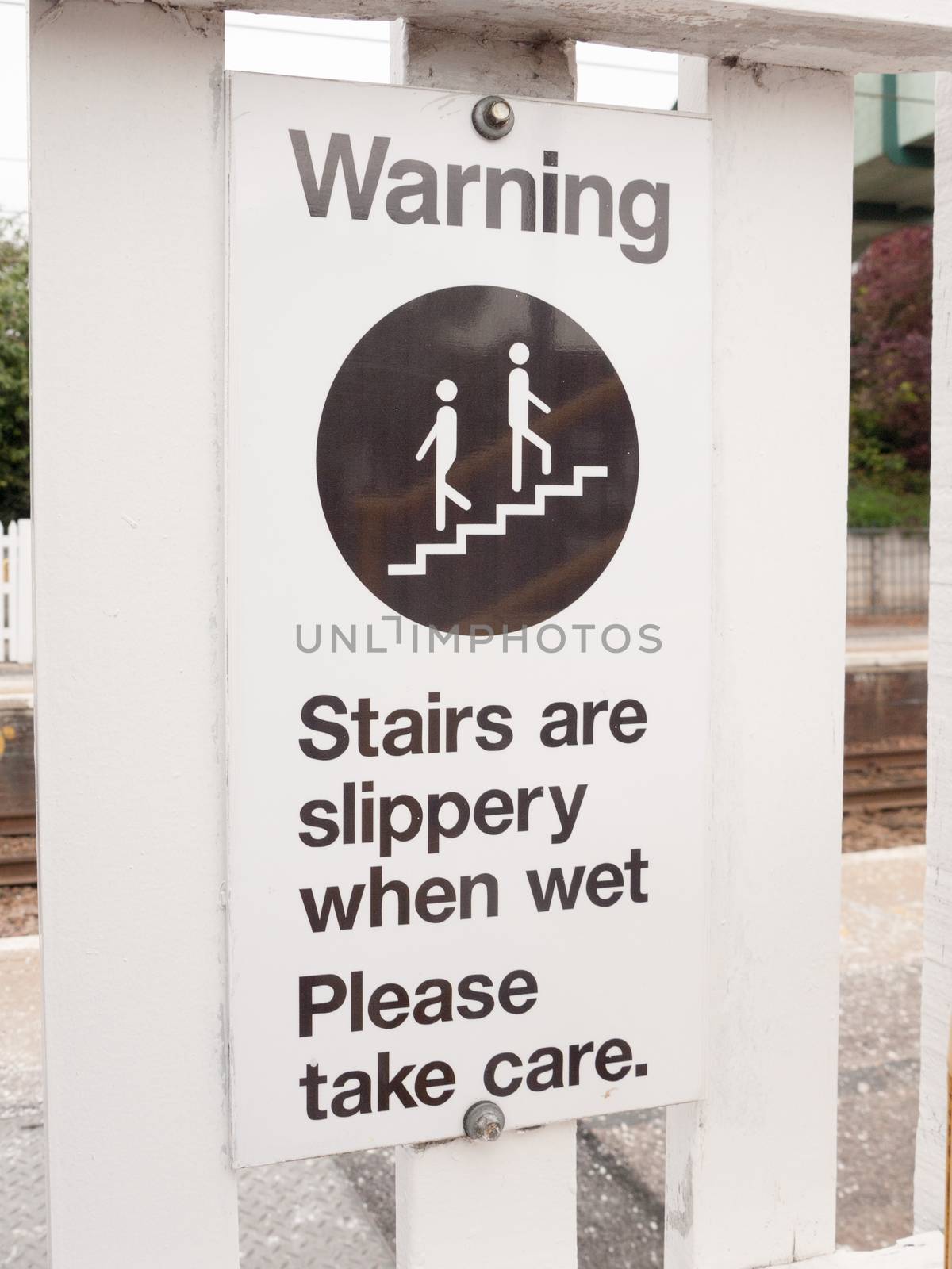 a warning sign saying stairs are slippery when wet please take care near train track bridge steps up careful safety caution advisory